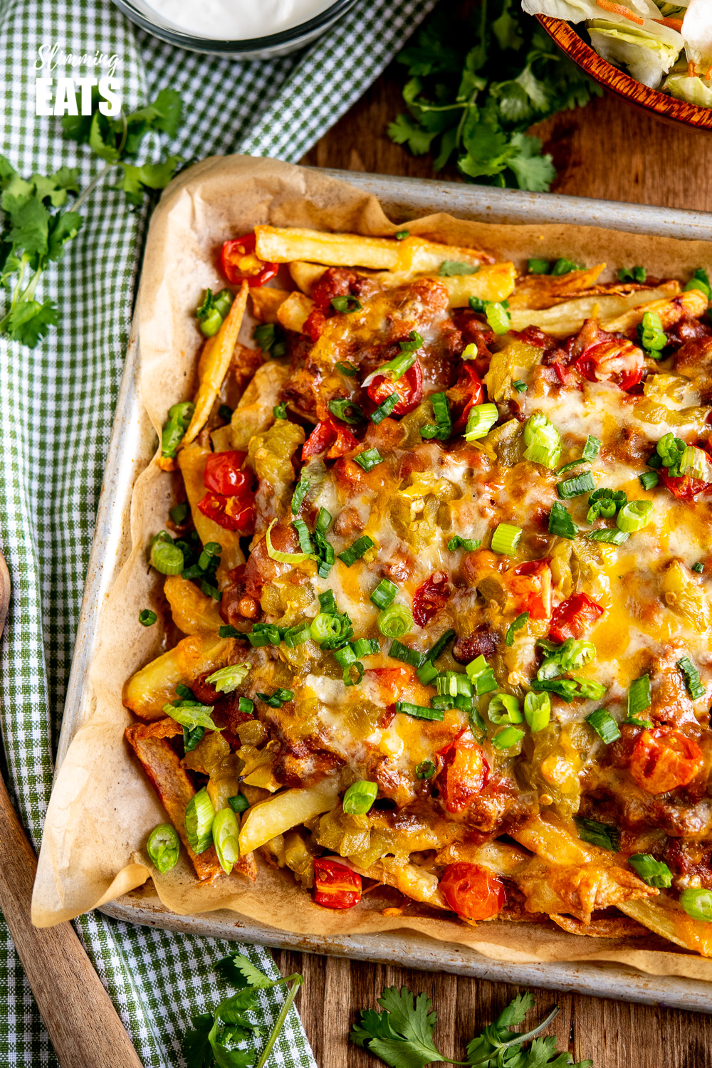 chilli cheese fries on a baking tray lined with parchment paper on wooden board with green checked fabric napkin