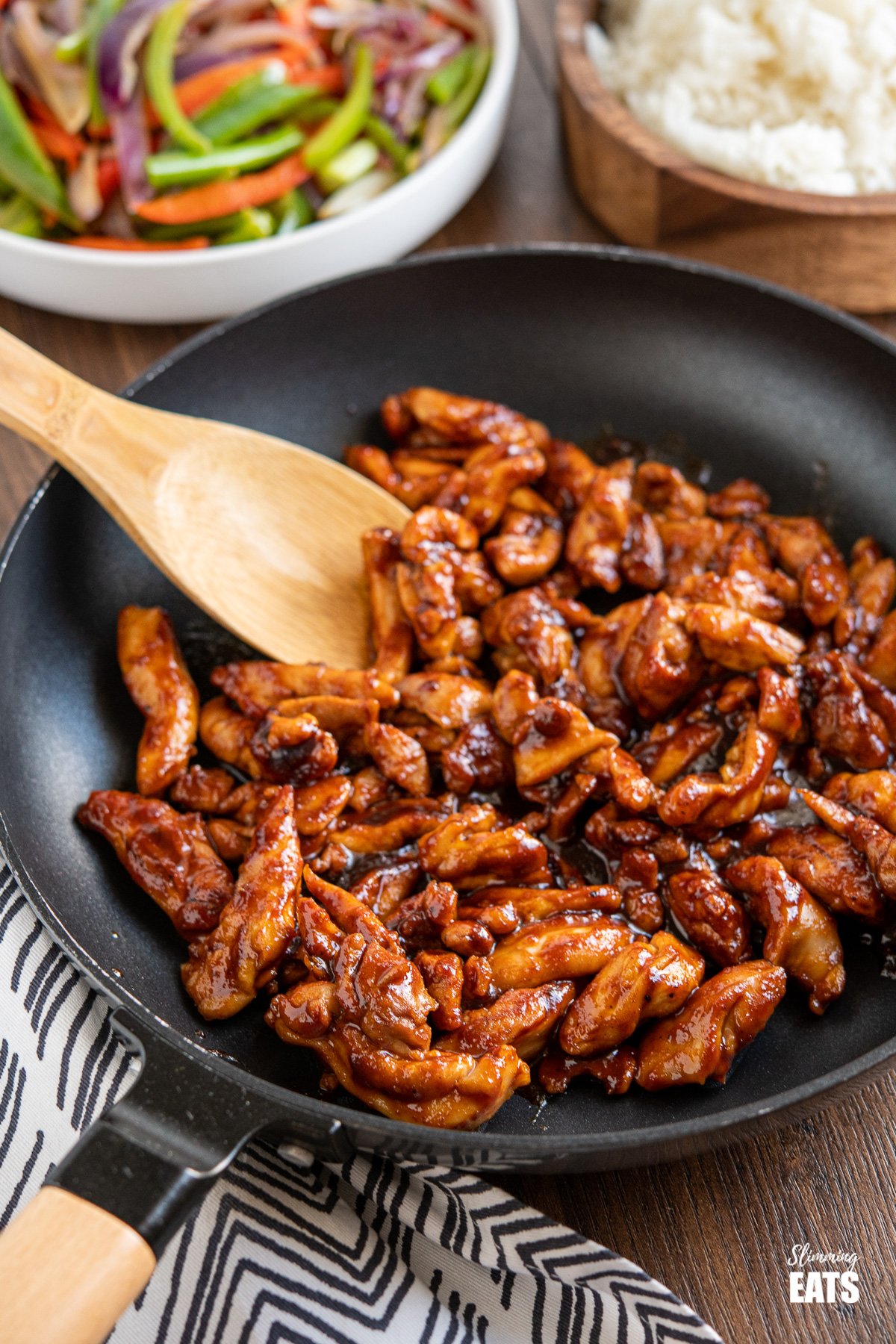 sweet and sticky chicken In frying pan with vegetables and rice in background