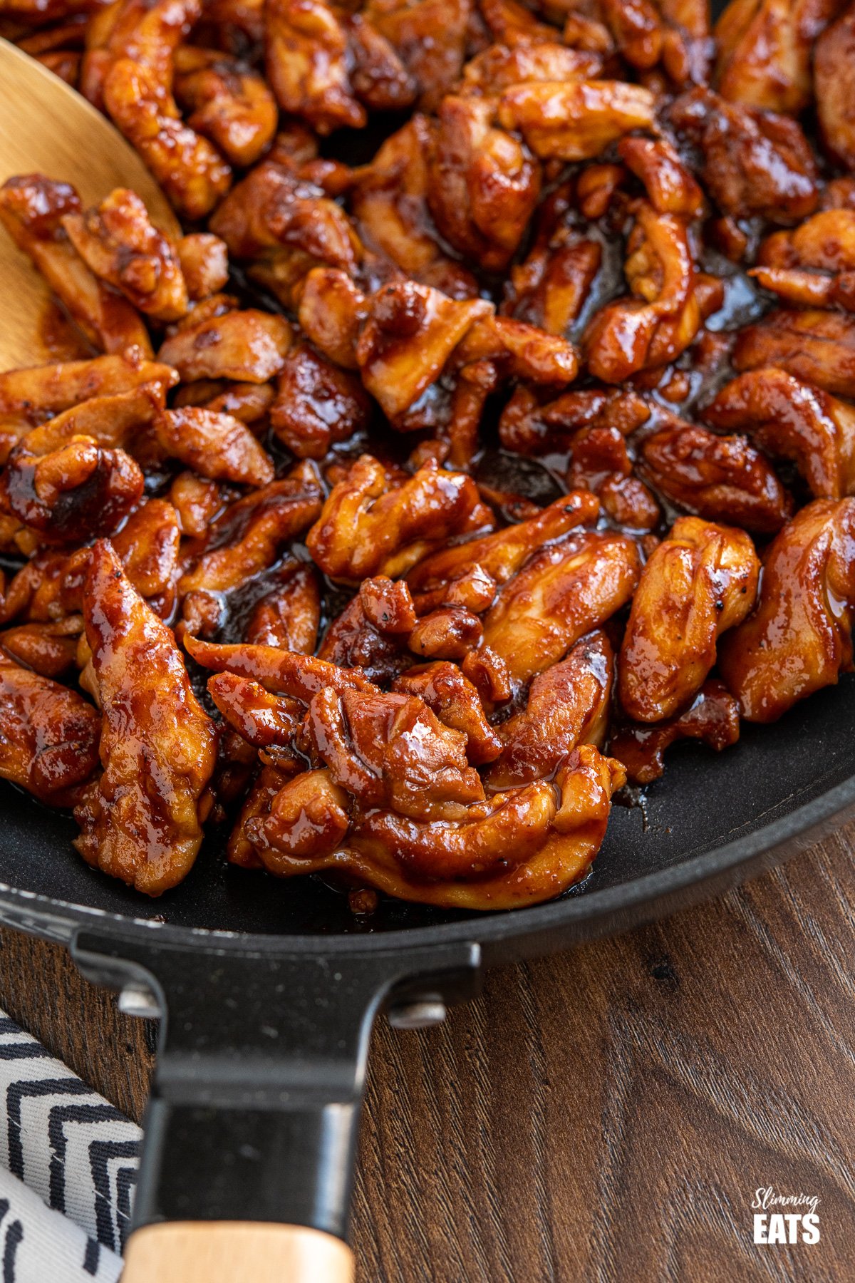 close up of sweet and sticky chicken in frying pan with wooden handle