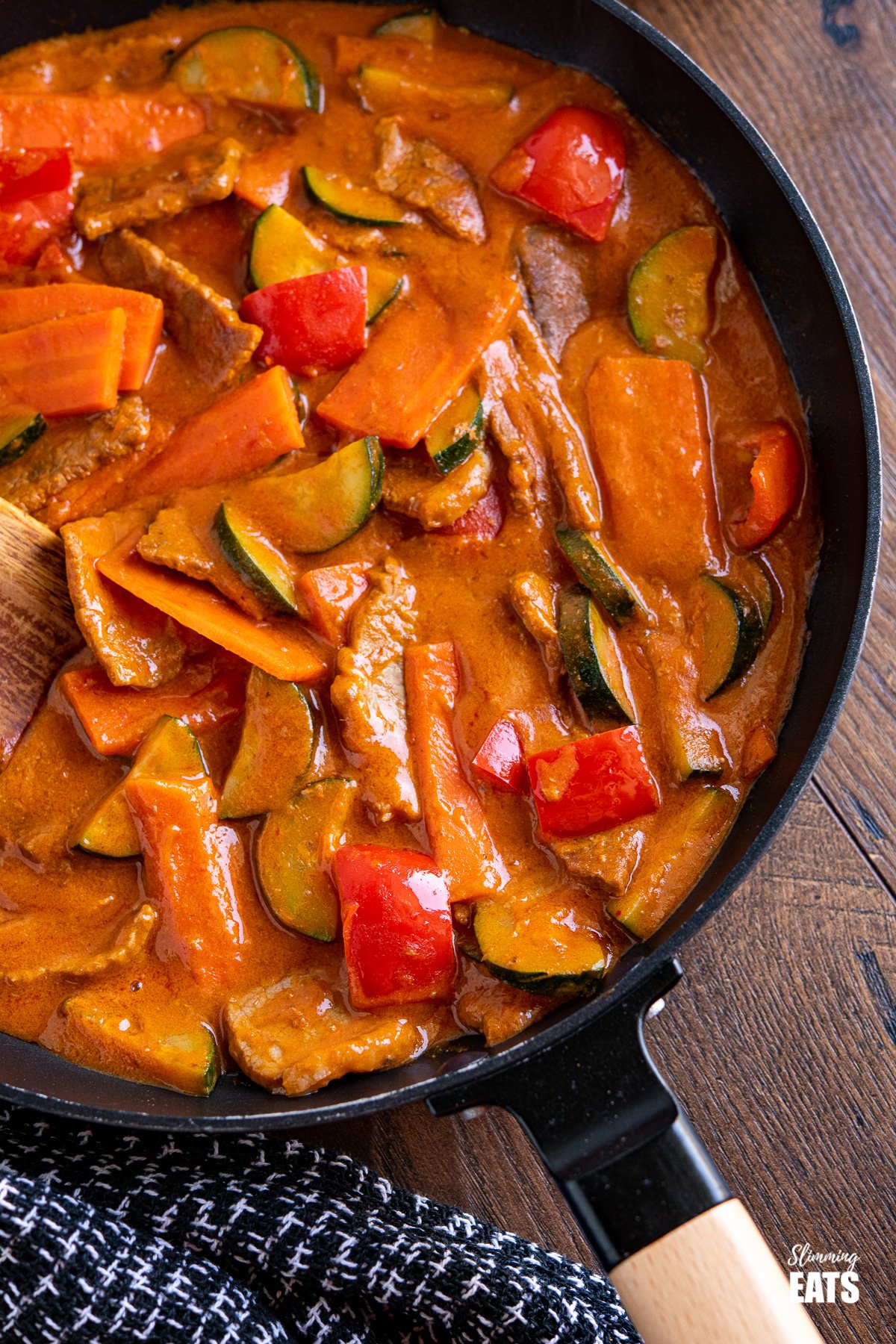 close up of thai red beef curry in black frying pan with wooden handle