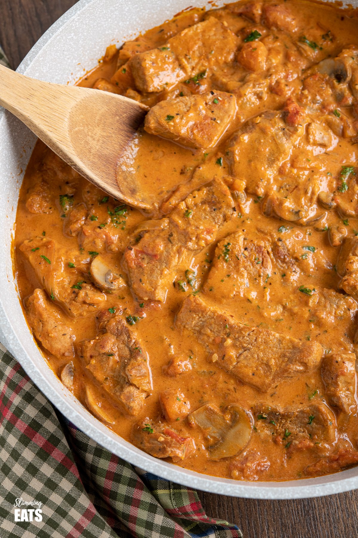 close up of Creamy Pork Casserole in deep frying pan with wooden spoon