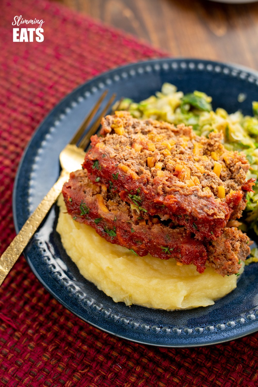 close up of 2 slices of beef and sweet potato meatloaf over mashed potatoes on a navy blue plate with gold fork. 