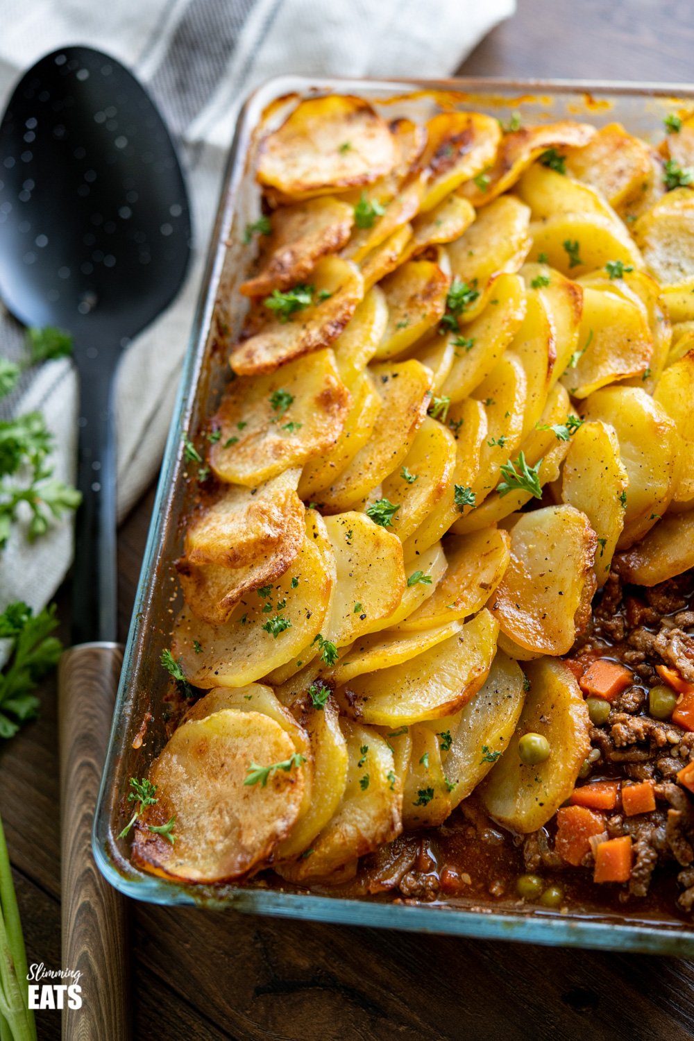 minced beef hotpot crispy potato topped pie in glass oven proof dish with spoon to the left. 