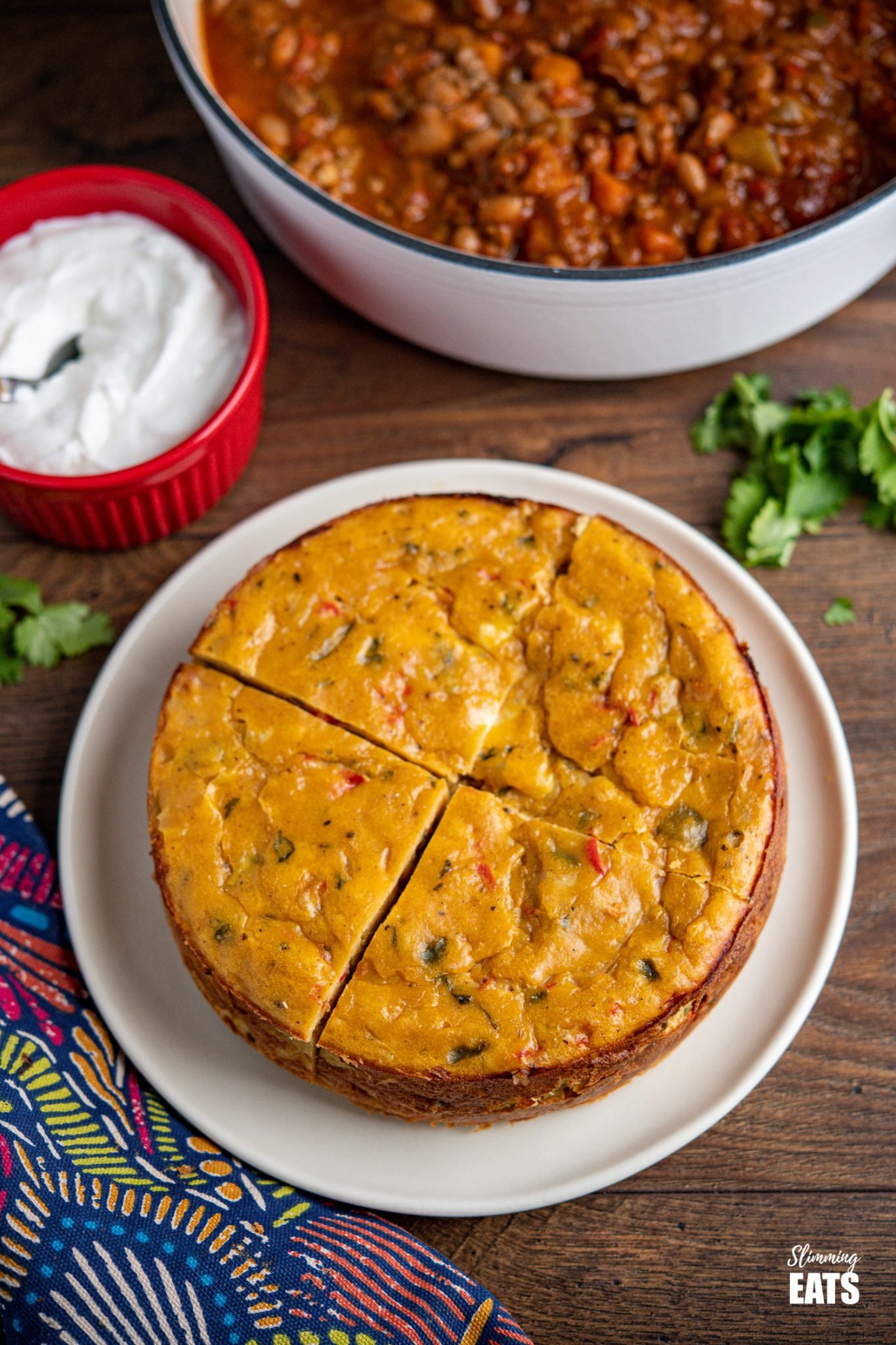 sliced lentil cheddar bake on plate with pan of chilli and soured cream in background