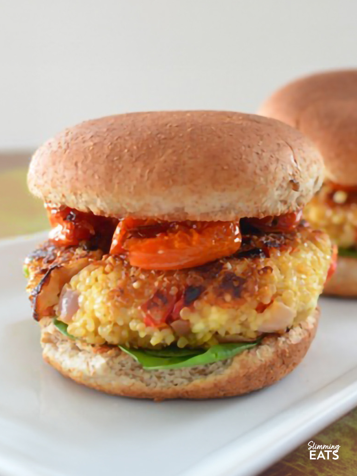 Roasted Red Pepper and Feta Quinoa Burgers in wholemeal buns with roasted balsamic tomatoes and spinach on a white plate