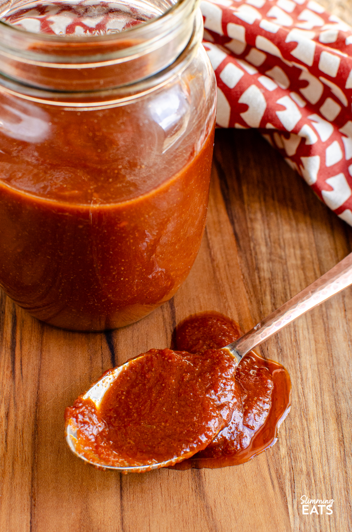 Homemade Barbecue Sauce in a jar on a board with a spoon with some of the sauce