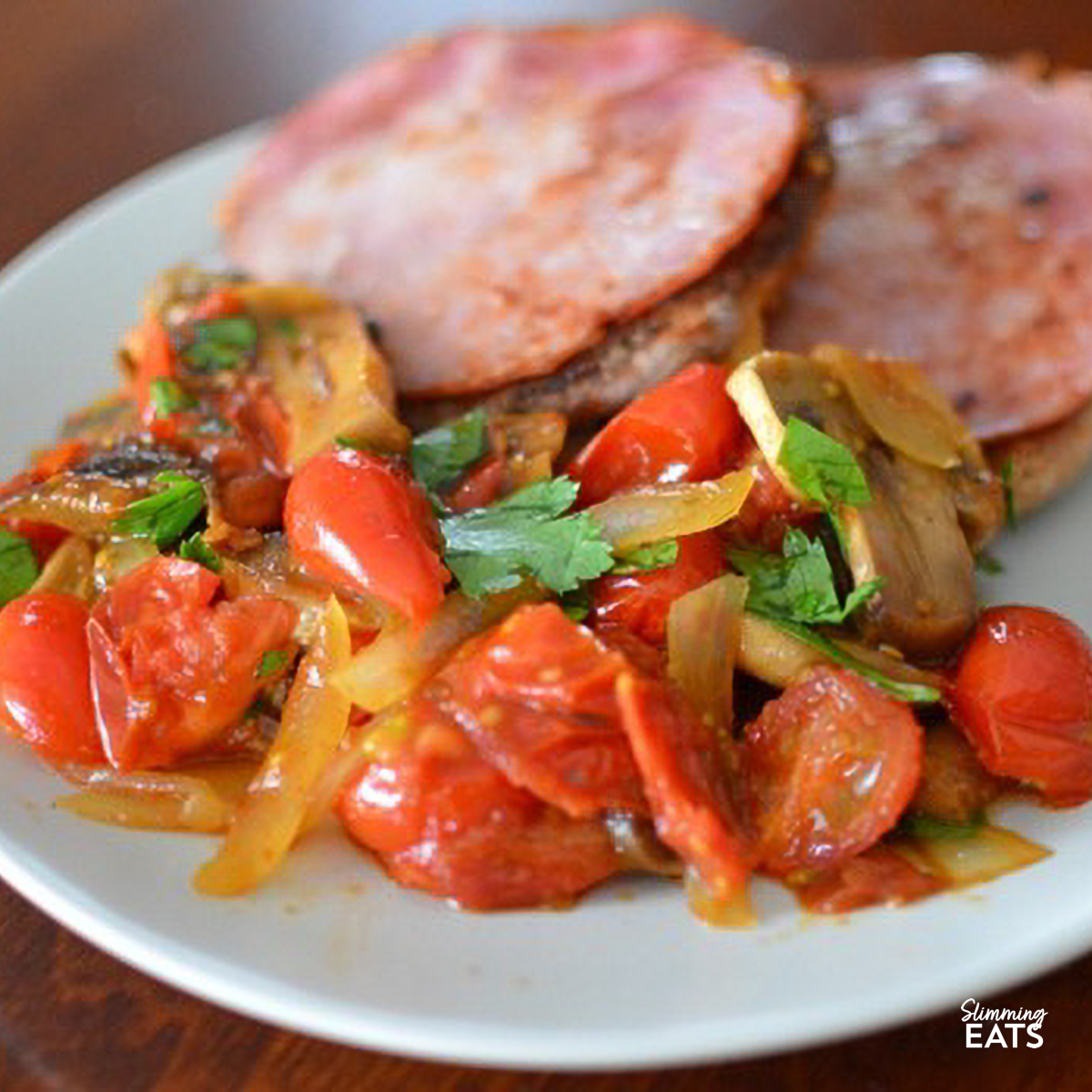 Golden pan-fried Canadian bacon atop toasted English muffins, accompanied by sautéed sweet tomatoes with onion and mushrooms, garnished with parsley.