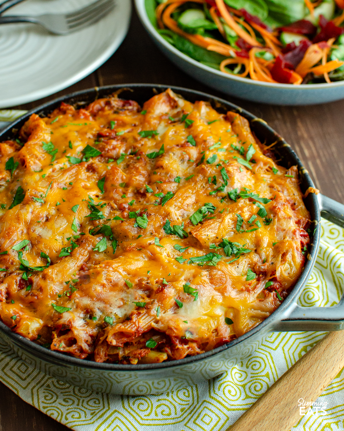 tuna pasta bake in staub grey cast iron skillet, with bowl of salad and plates in background.
