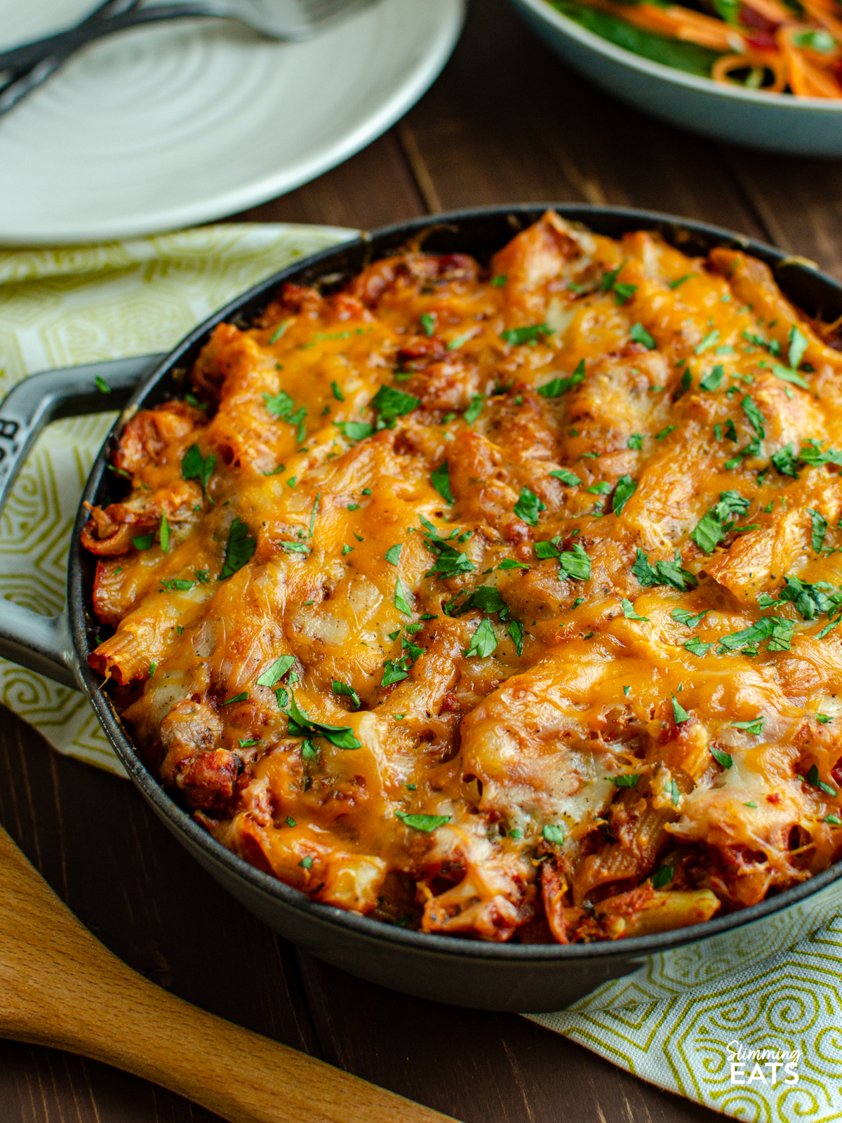 tuna pasta bake in staub grey cast iron skillet, with bowl of salad and plates in background.