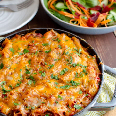 tuna pasta bake in cast iron skillet with salad and white plate in background