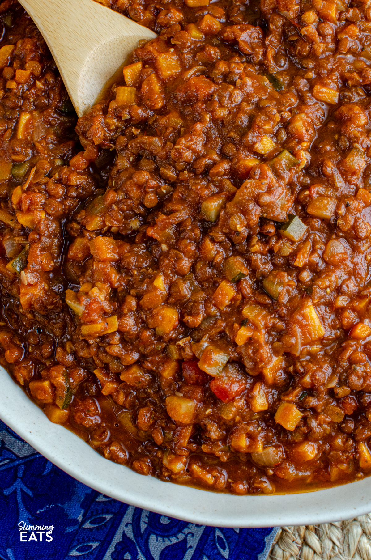 Lentil Bolognese - a hearty comforting meat free bolognese packed with lentils, vegetables and rich tomato flavour that is perfect for family dinners and batch cooking. It is filling, budget friendly and a great way to turn a simple bag of lentils into something really delicious. close up of Lentil Bolognese in a round dish with wooden spoon
