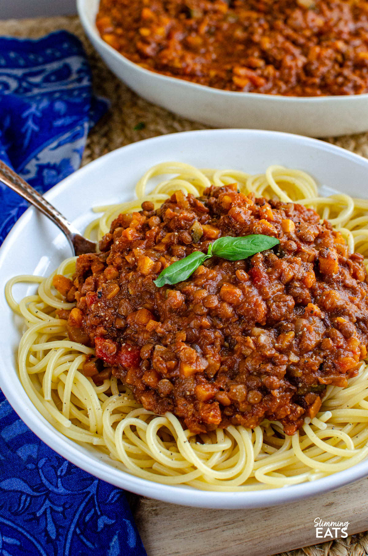 Lentil Bolognese - a hearty comforting meat free bolognese packed with lentils, vegetables and rich tomato flavour that is perfect for family dinners and batch cooking. It is filling, budget friendly and a great way to turn a simple bag of lentils into something really delicious. Lentil Bolognese over spaghetti in a white bowl garnish with a couple of fresh basil leaves.