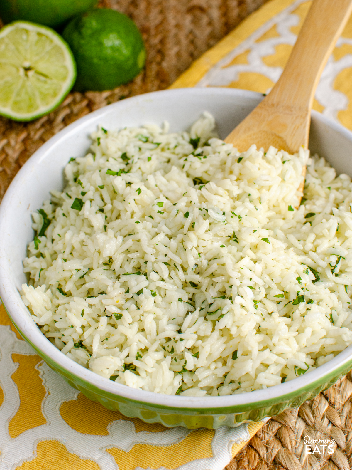 lime cilantro rice in a white and lime green bowl with wooden spoon, limes visible in background
