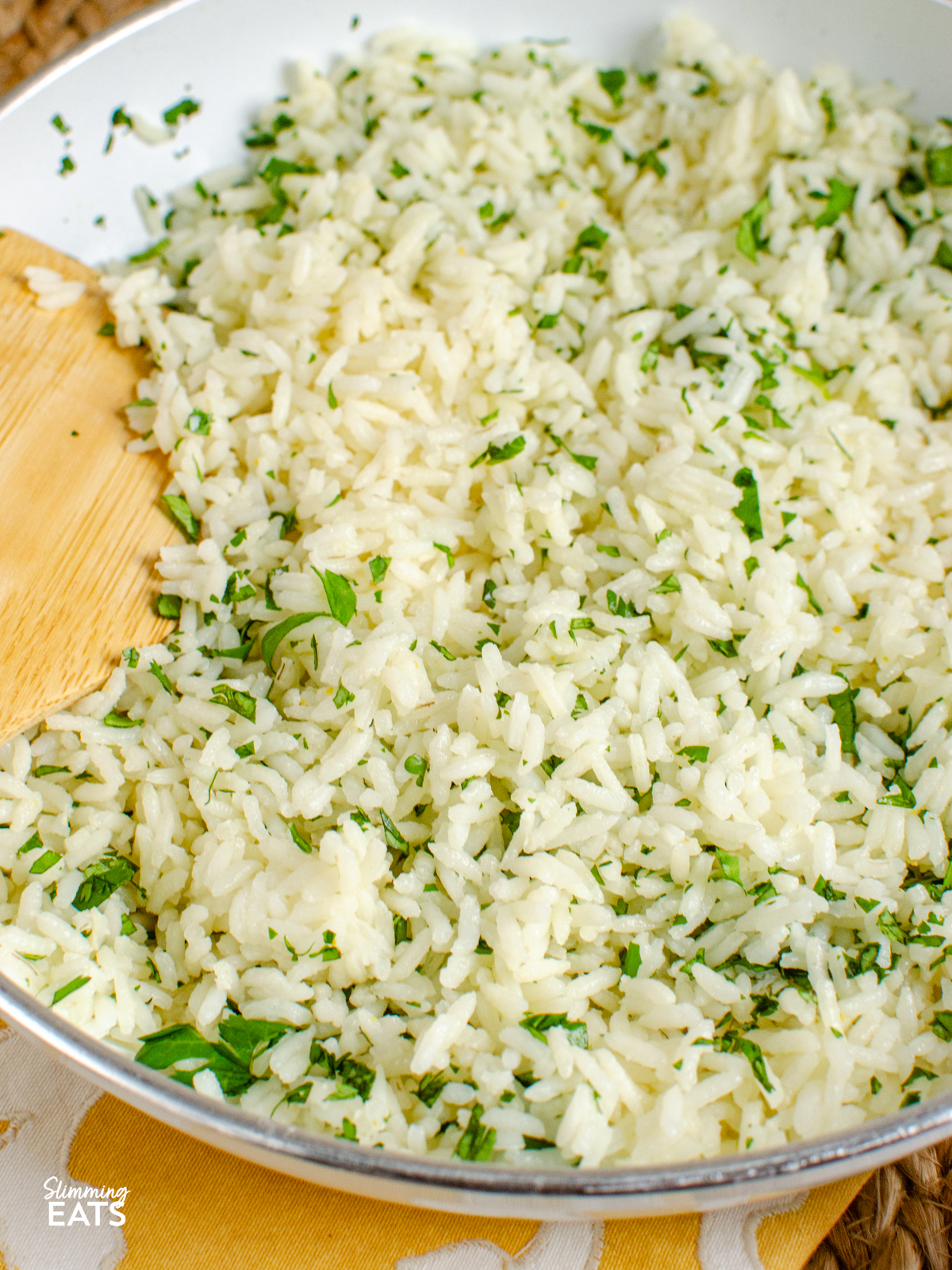 close up of lime cilantro rice in a white non stick frying pan with wooden spoon