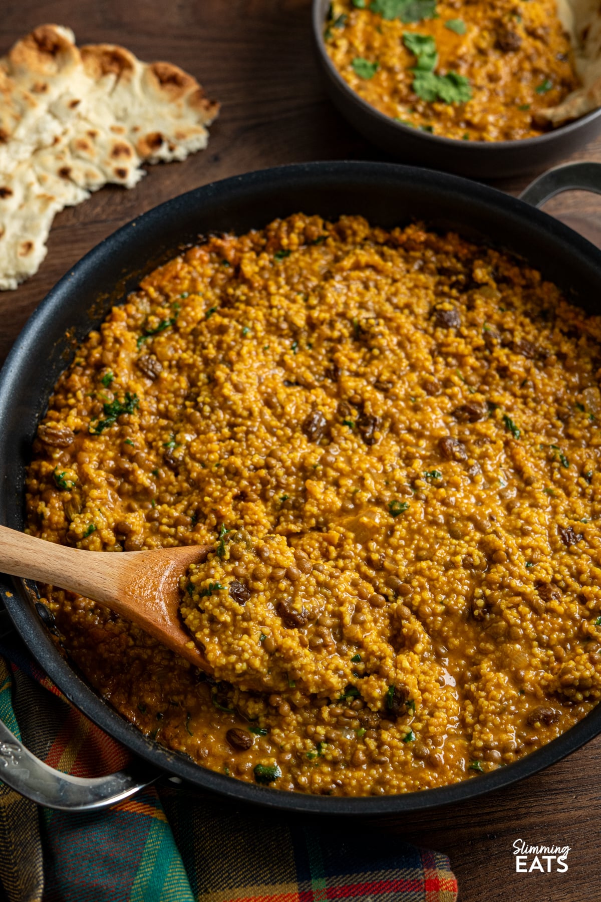 Coconut Millet and Lentil Curry in a double handled non stick skillet with small bowl filled with curry and torn naan next to pan
