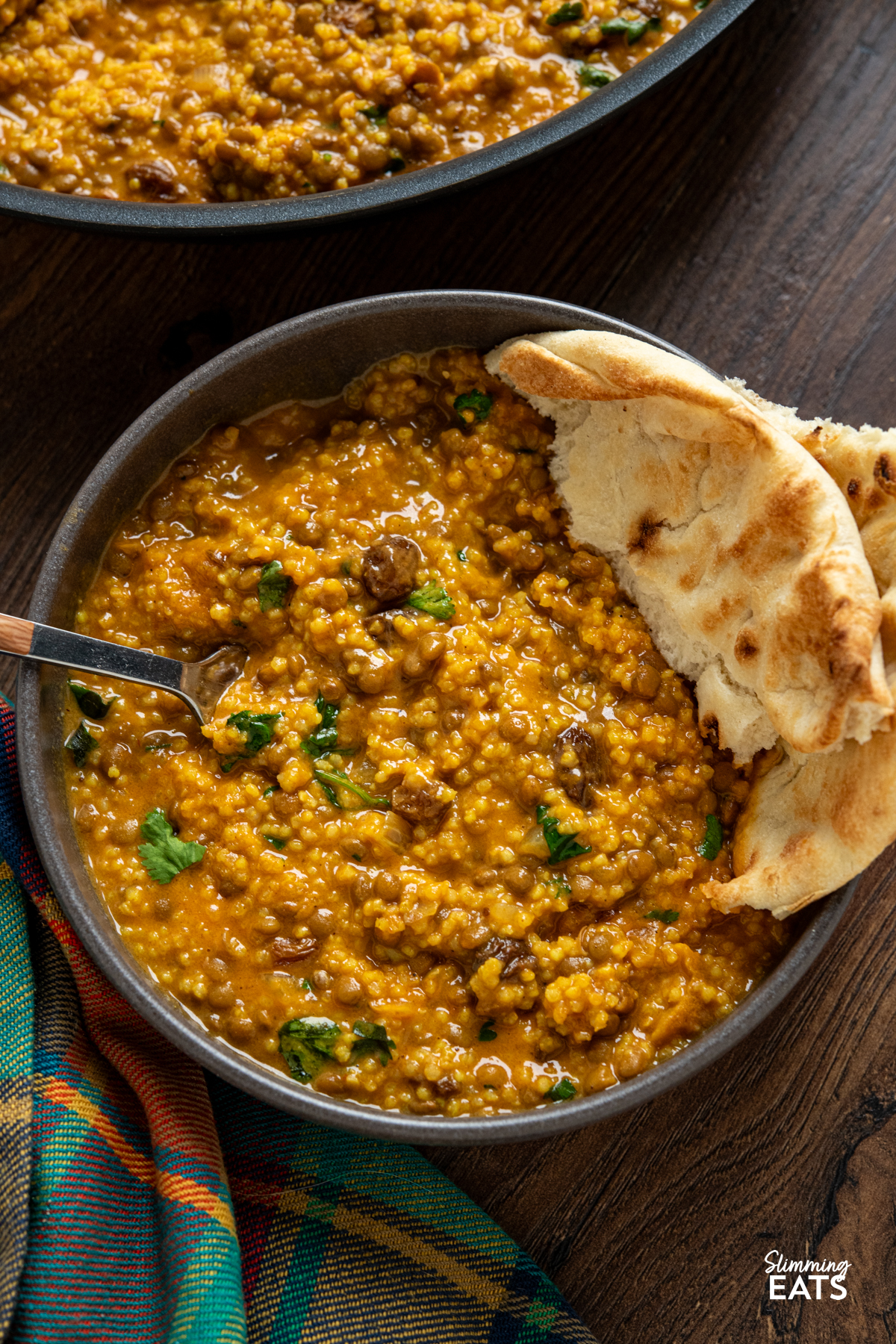 Coconut Millet and Lentil Curry in a small grey bowl with torn naan and wooden handled fork placed in bowl