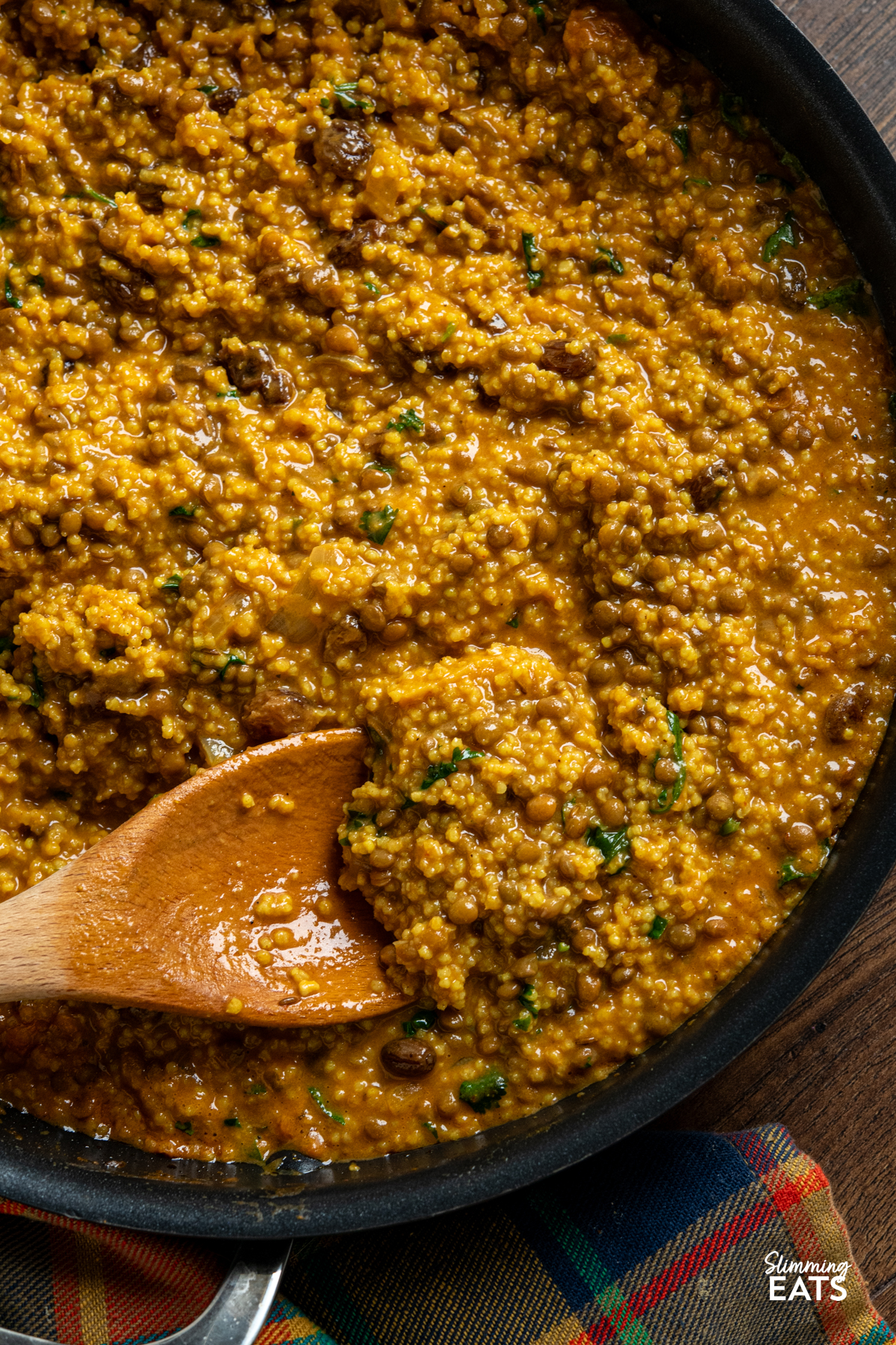 close up of Coconut Millet and Lentil Curry in a double handled non stick skillet with wooden spoon