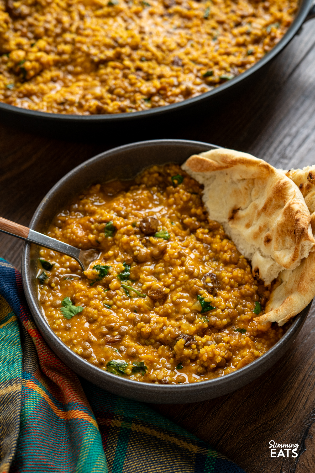 Coconut Millet and Lentil Curry in a small grey bowl with torn naan and wooden handled fork placed in bowl