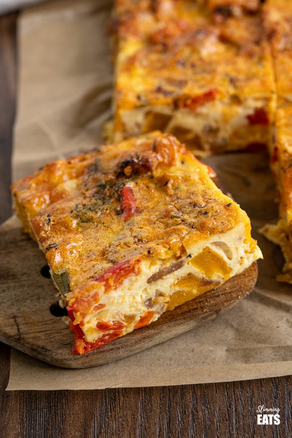 close up of slice of roasted butternut squash and red pepper quiche on parchment paper