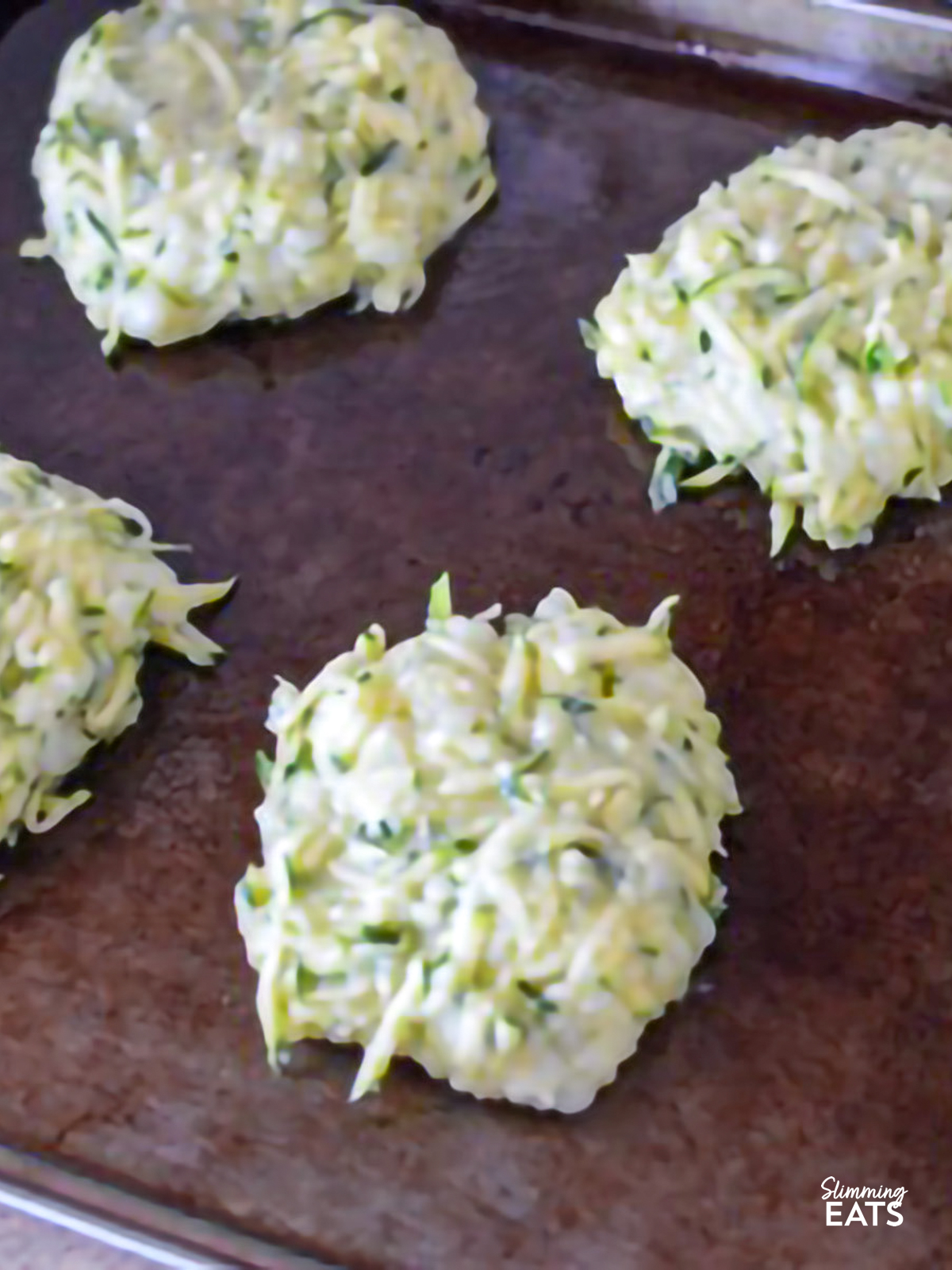 Rustic Courgette and Potato Cakes on a white rectangle plate on a baking tray ready to be baked
