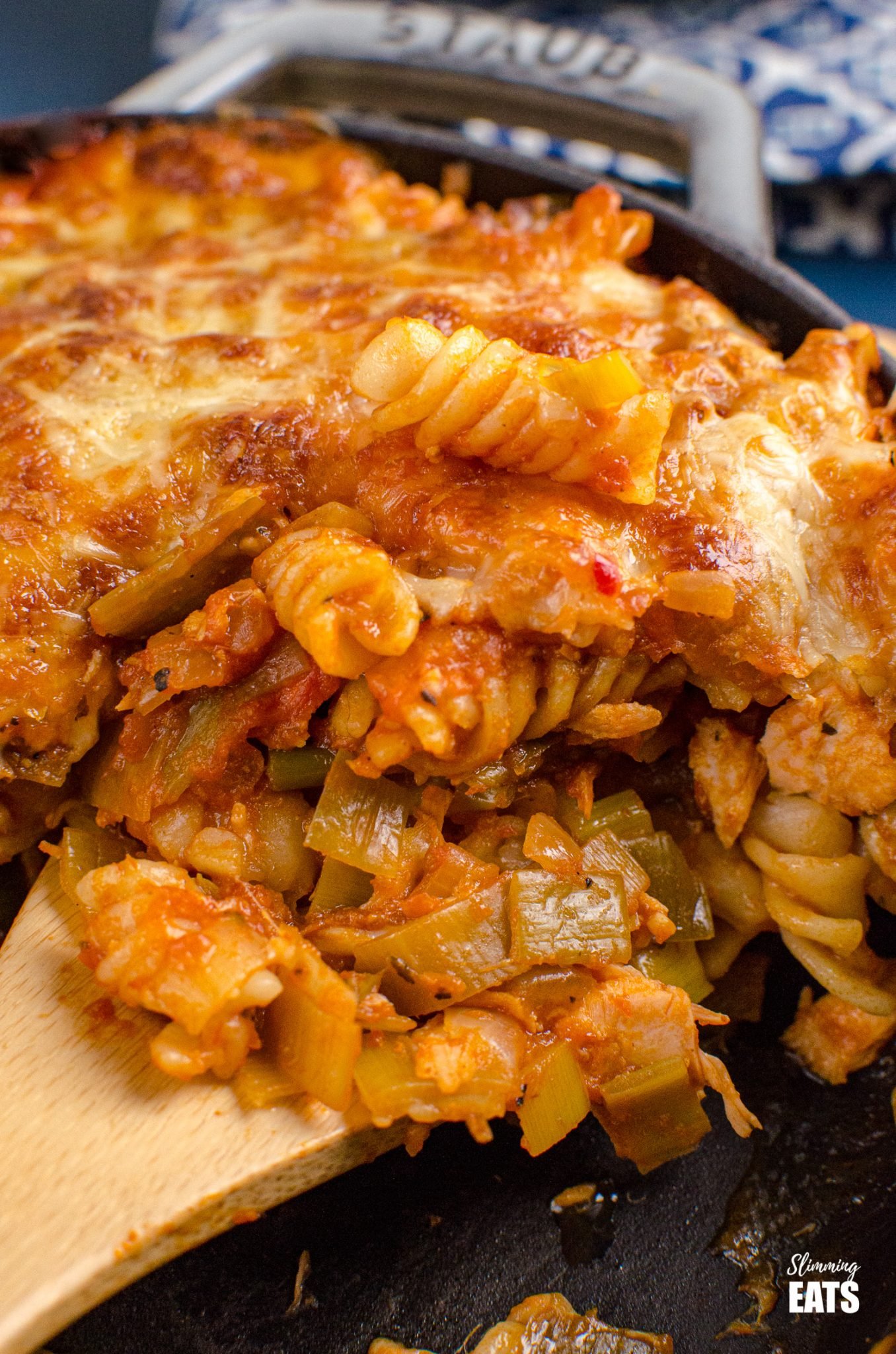 Salmon and Leek Pasta Bake - Salmon and Leek Pasta Bake - a delicious recipe using fresh salmon, sauteed leeks and a homemade tomato pasta sauce, all finished off with melted cheesy goodness - yum!! Slimming World and Weight Watchers friendly close up of wooden spoon scooping up Salmon and Leek Pasta Bake from grey cast iron Staub skillet
