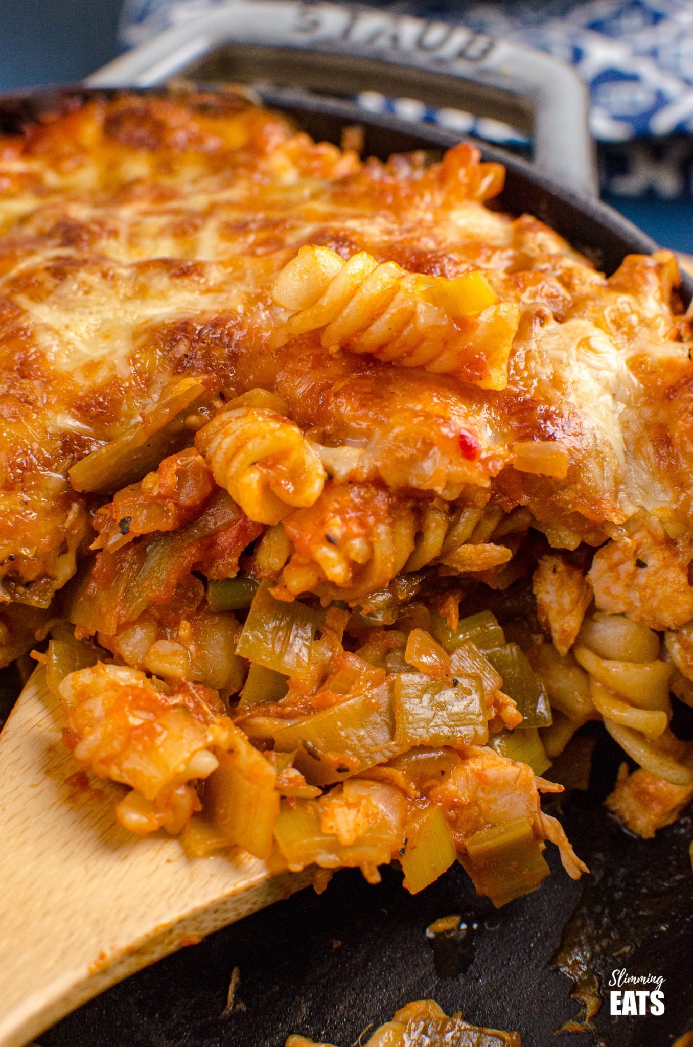 close up of wooden spoon scooping up Salmon and Leek Pasta Bake from grey cast iron Staub skillet 