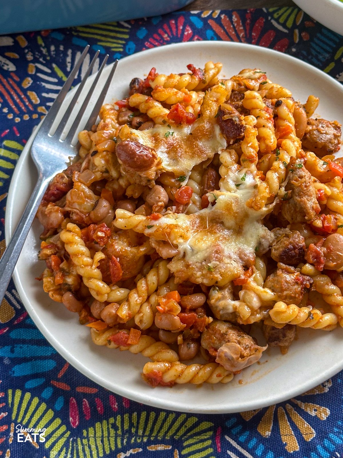 Impress the whole family with this delicious Sausage and Bean Pasta Bake! Packed with all the flavours everyone loves—sausages, beans, and pasta—this dish is both satisfying and simple to make. It's a firm favourite with my kids, who can’t get enough of it, and it’s perfect for both adults and little ones alike. close up of a portion of Sausage and Bean Pasta Bake served up on a white plate with fork to the side