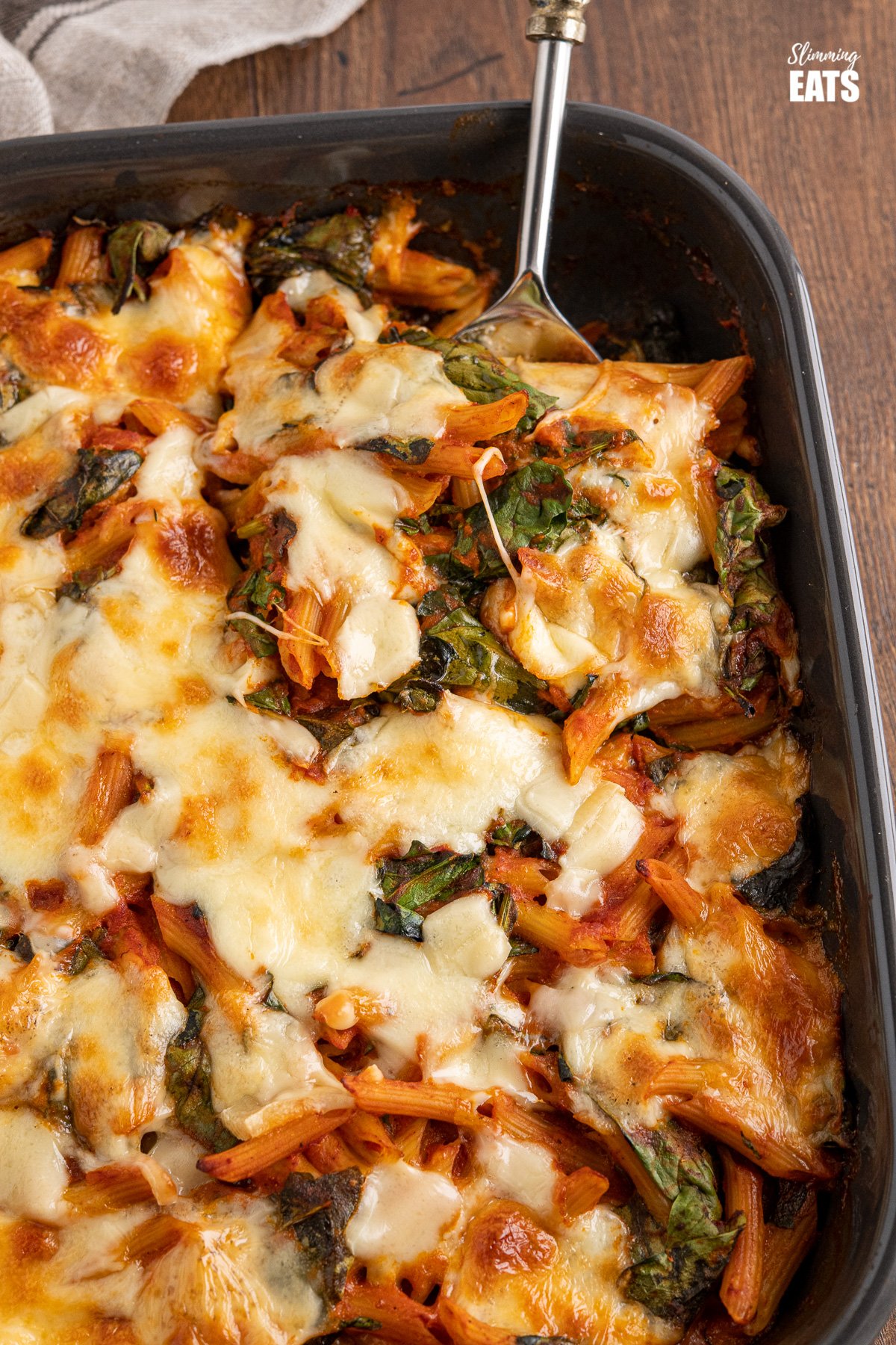 close up of spinach pasta bake with spoon in dark grey oven dish