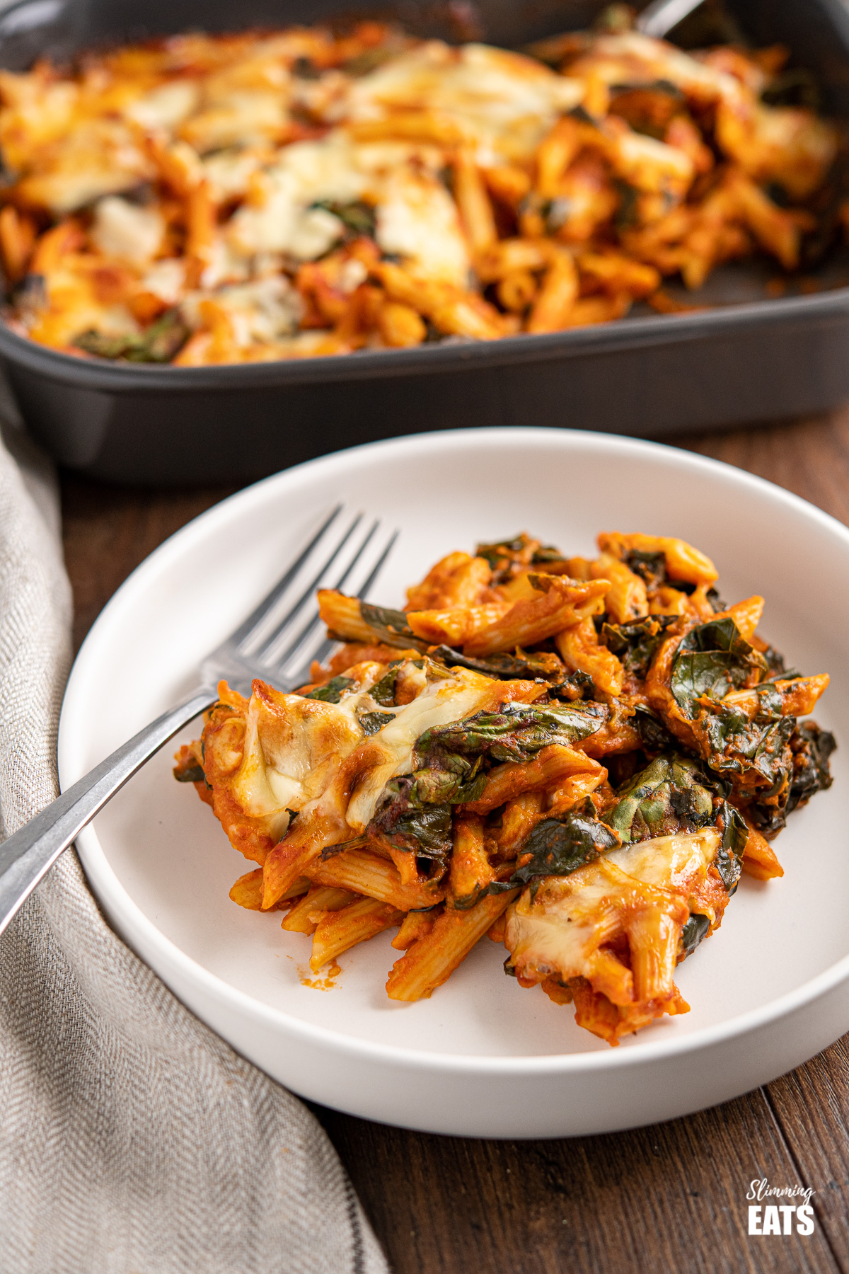 white plate with a serving of spinach pasta bake, oven dish in background