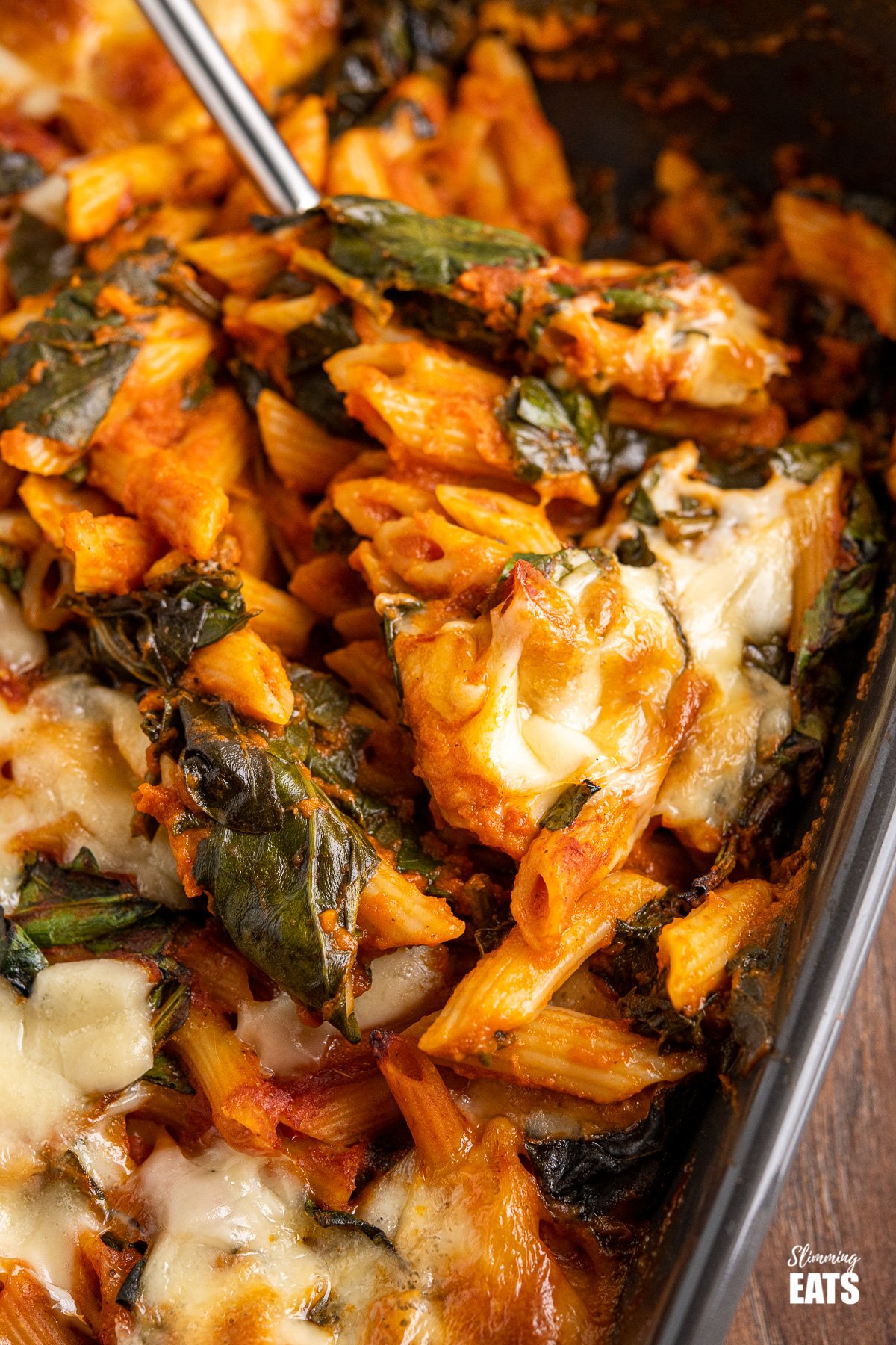 spoon dishing up spinach pasta bake from dark grey oven dish