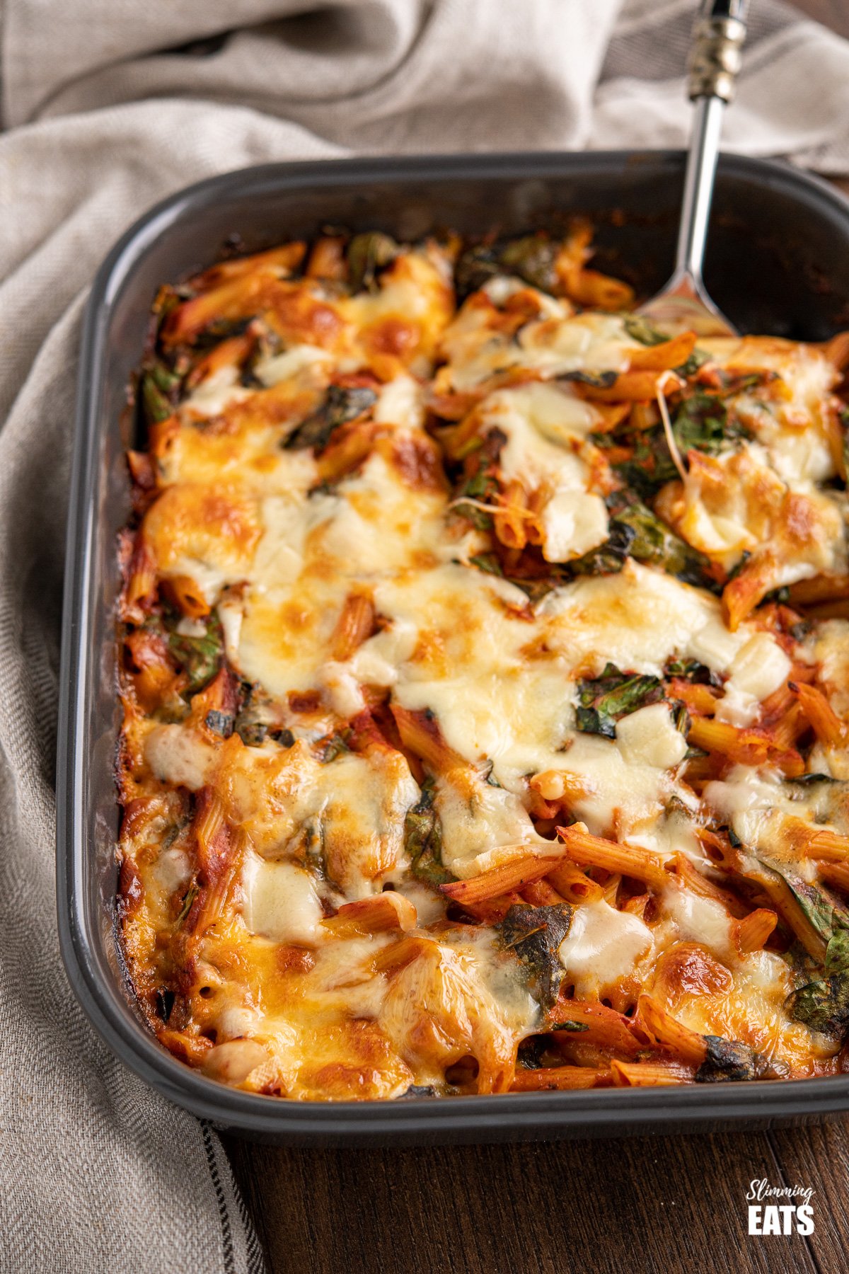 spinach pasta bake with spoon in dark grey oven dish