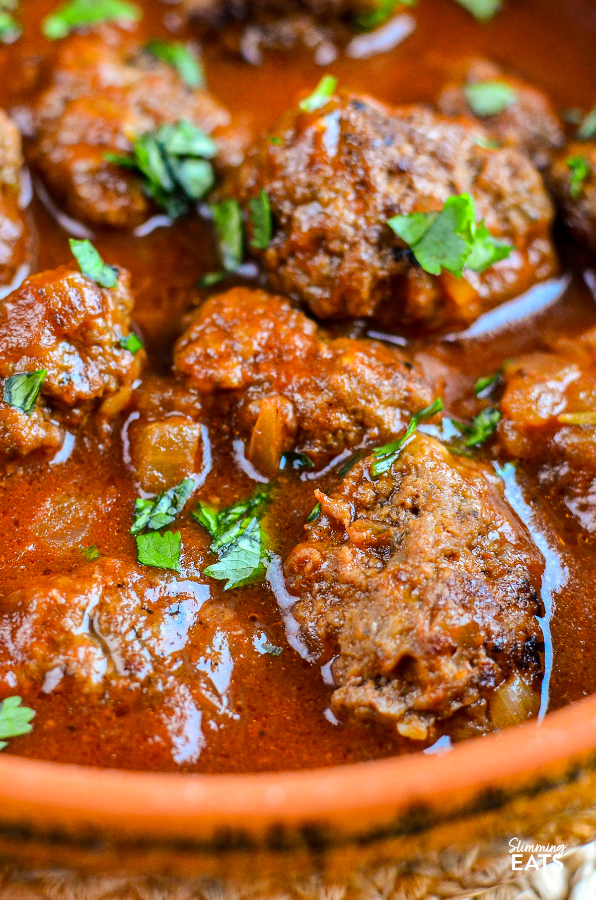 Beef meatballs bathed in a rich tomato-maple sauce, presented in an orange ceramic dish with a handle, showcasing a vibrant and appetizing meal.