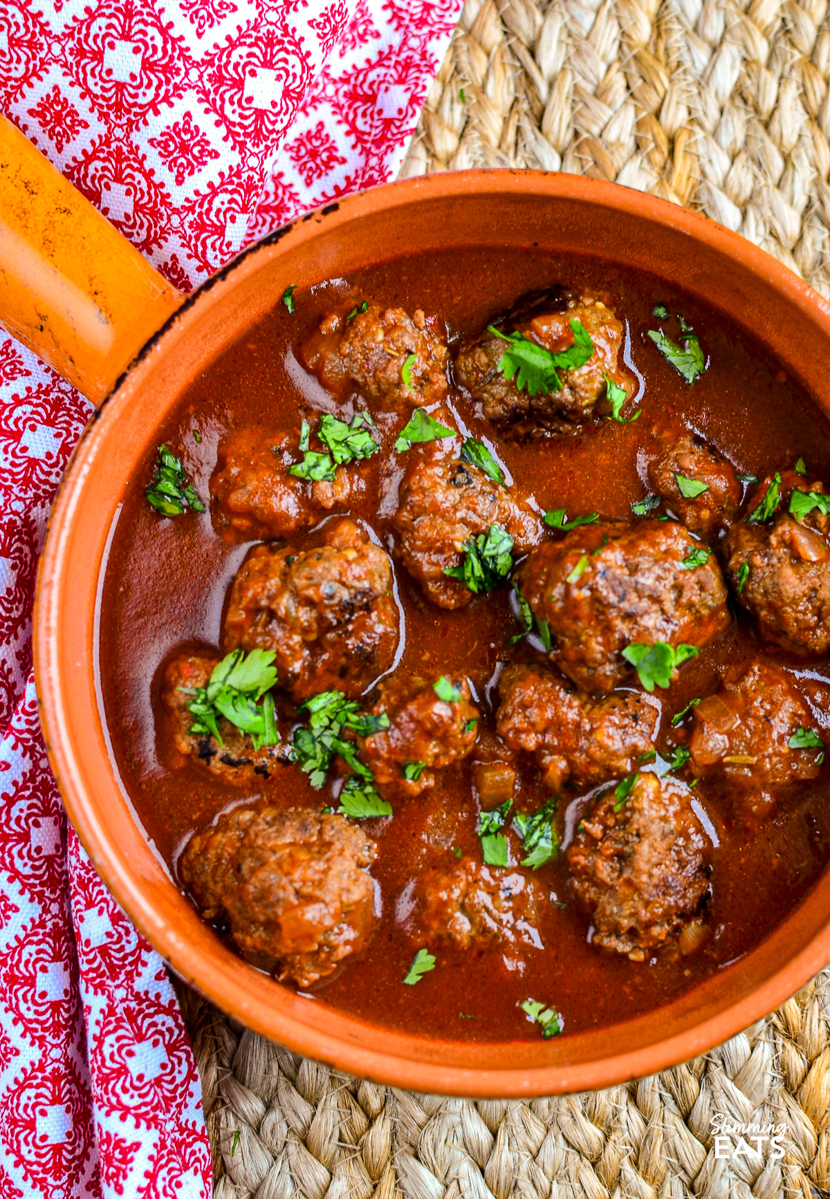Beef meatballs bathed in a rich tomato-maple sauce, presented in an orange ceramic dish with a handle, showcasing a vibrant and appetizing meal.