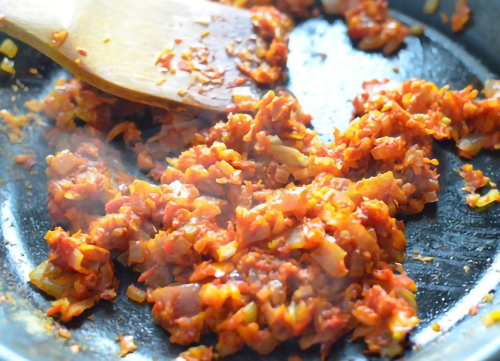 ONIONS, PEPPERS AND GARLIC BEING SAUTEED IN A PAN WITH SPICES AND TOMATO PASTE