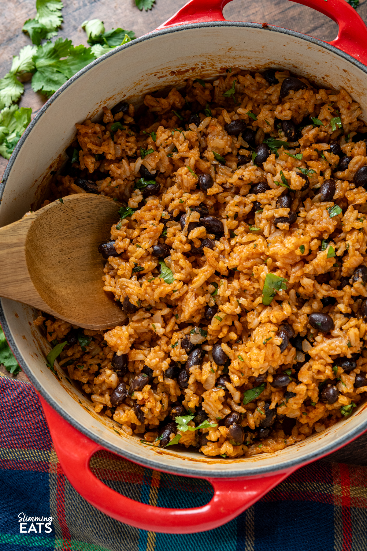 Mexican Rice - a flavour packed rice dish with spicy tomato flavours, black beans and a little kick of jalapeño that makes the perfect side for all your favourite Mexican inspired meals. It is easy to make, full of colour and delicious enough to enjoy all on its own. Mexican rice in cerise cast iron pot with wooden spoon scattered cilantro around pot