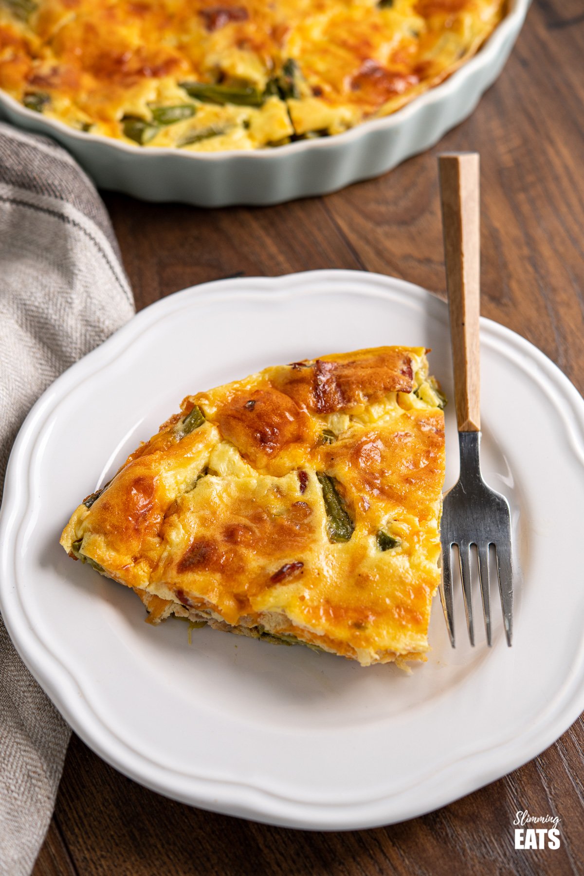 Crustless Asparagus and Bacon Quiche (from www.slimmingeats.com) - a perfect recipe for lunches and picnics using fresh asparagus, with the delicious addition of smokey bacon and melted cheesy goodness. Gluten Free, Slimming World and Weight Watchers friendly slice of Crustless Asparagus and Bacon Quiche on white plate with wooden handles fork.