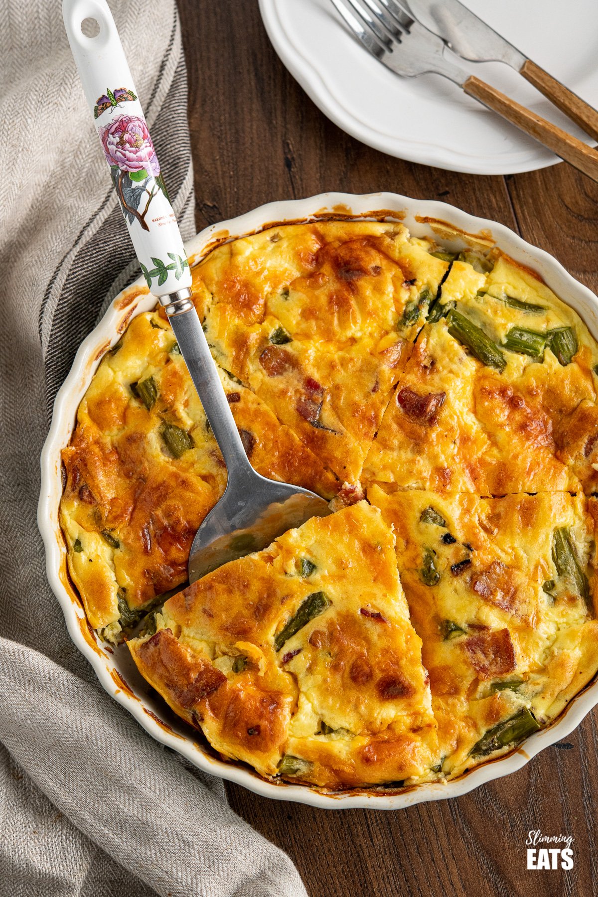 Crustless Asparagus and Bacon Quiche in flan dish with spatula on wooden board