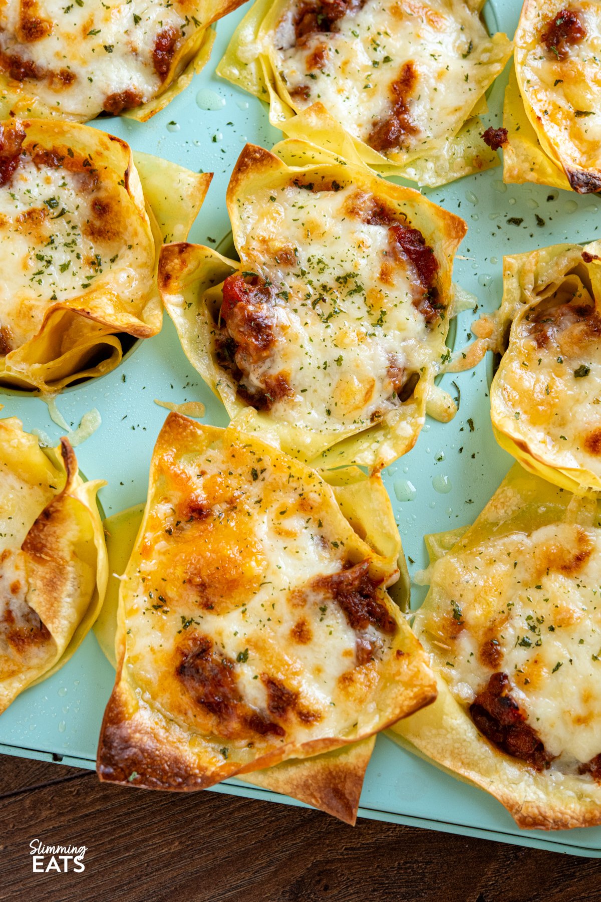 These Mini Lasagne Cups take all the best bits of a classic lasagne and reimagine them into perfectly portioned bites. Instead of layers, cooked lasagne sheets are shaped into little cups and stuffed with a rich, speedy bolognese. Topped with a light béchamel-style sauce and a scattering of cheese, they bake into golden-topped bundles of comfort the whole family will love. close up of Mini Lasagne Cups in a blue muffin tray