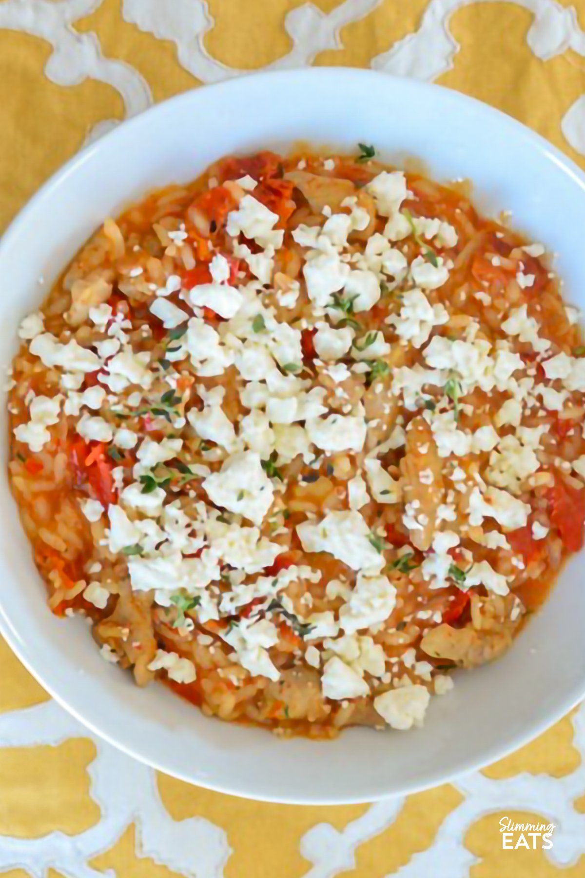 This Chicken, Roasted Red Pepper, and Sun-Dried Tomato Risotto combines rice with smoky peppers, savoury chicken, and tangy feta for a satisfying and flavourful meal. Chicken, Roasted Red Pepper, Sun-Dried Tomato Risotto with Crumbled Feta in a white bowl on a yellow and white placemat