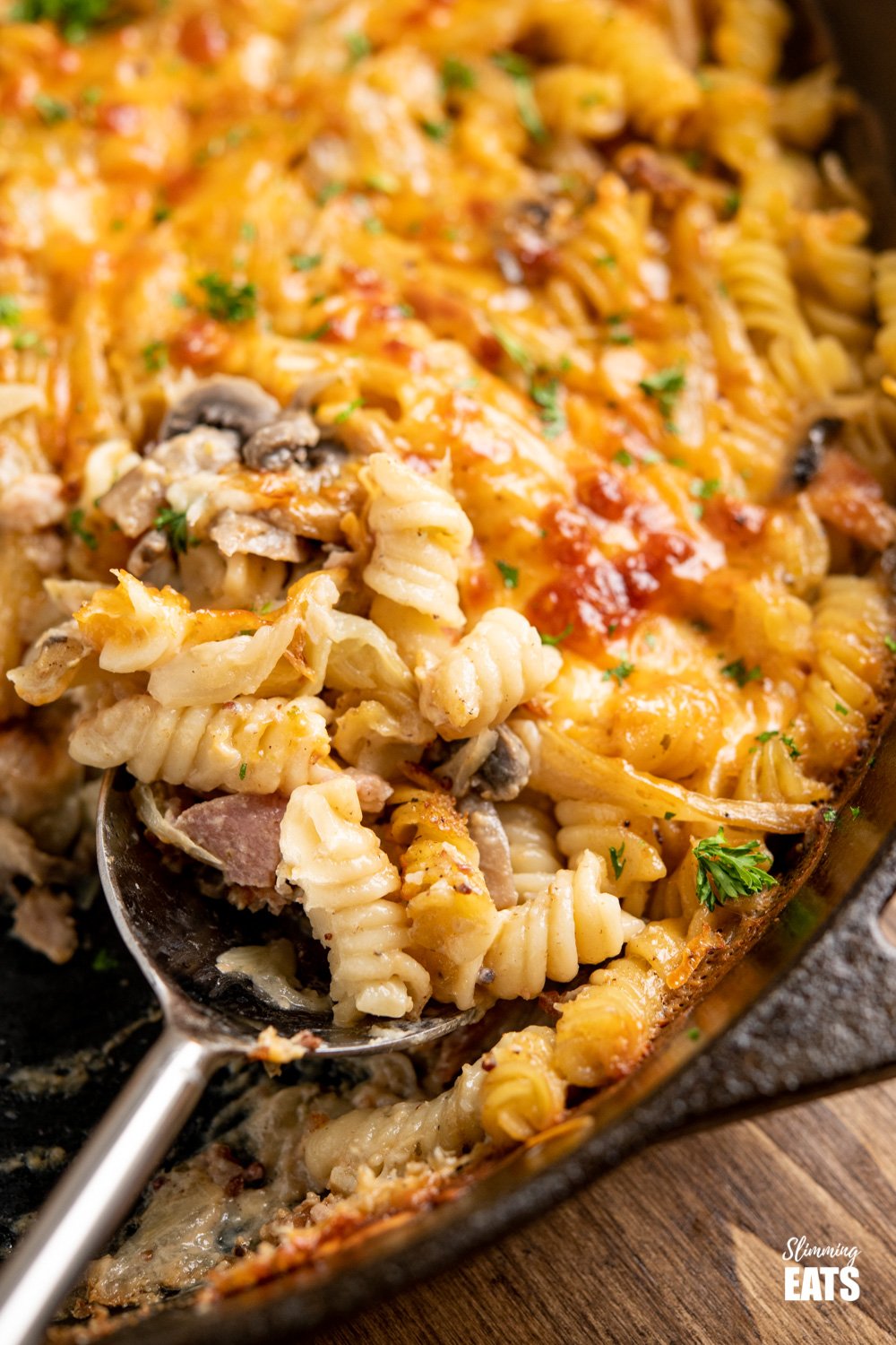 metal spoon scooping Bacon, Fennel and Mushroom Pasta Bake from cast iron skillet