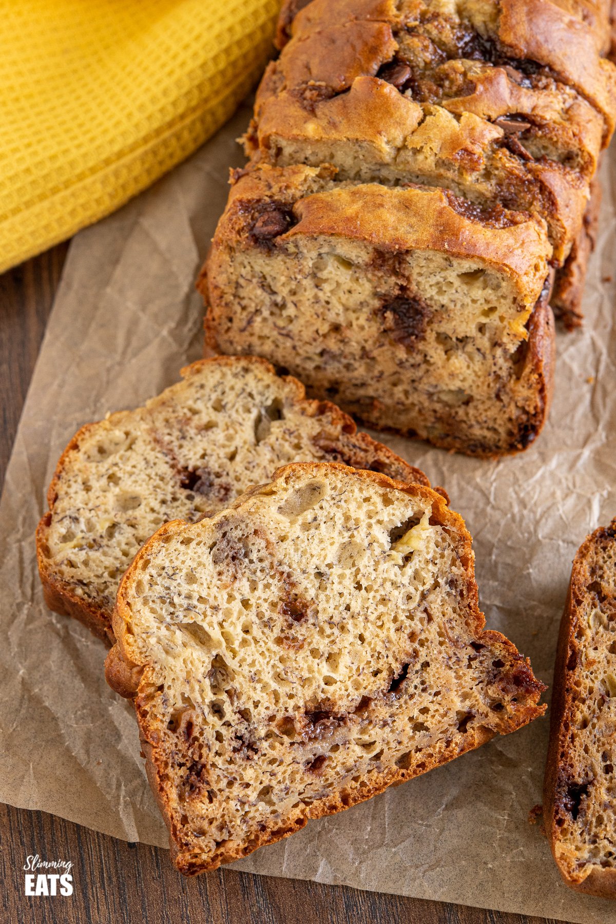 Sliced Healthy Banana and Chocolate Chip Loaf on parchment paper with yellow tea towel