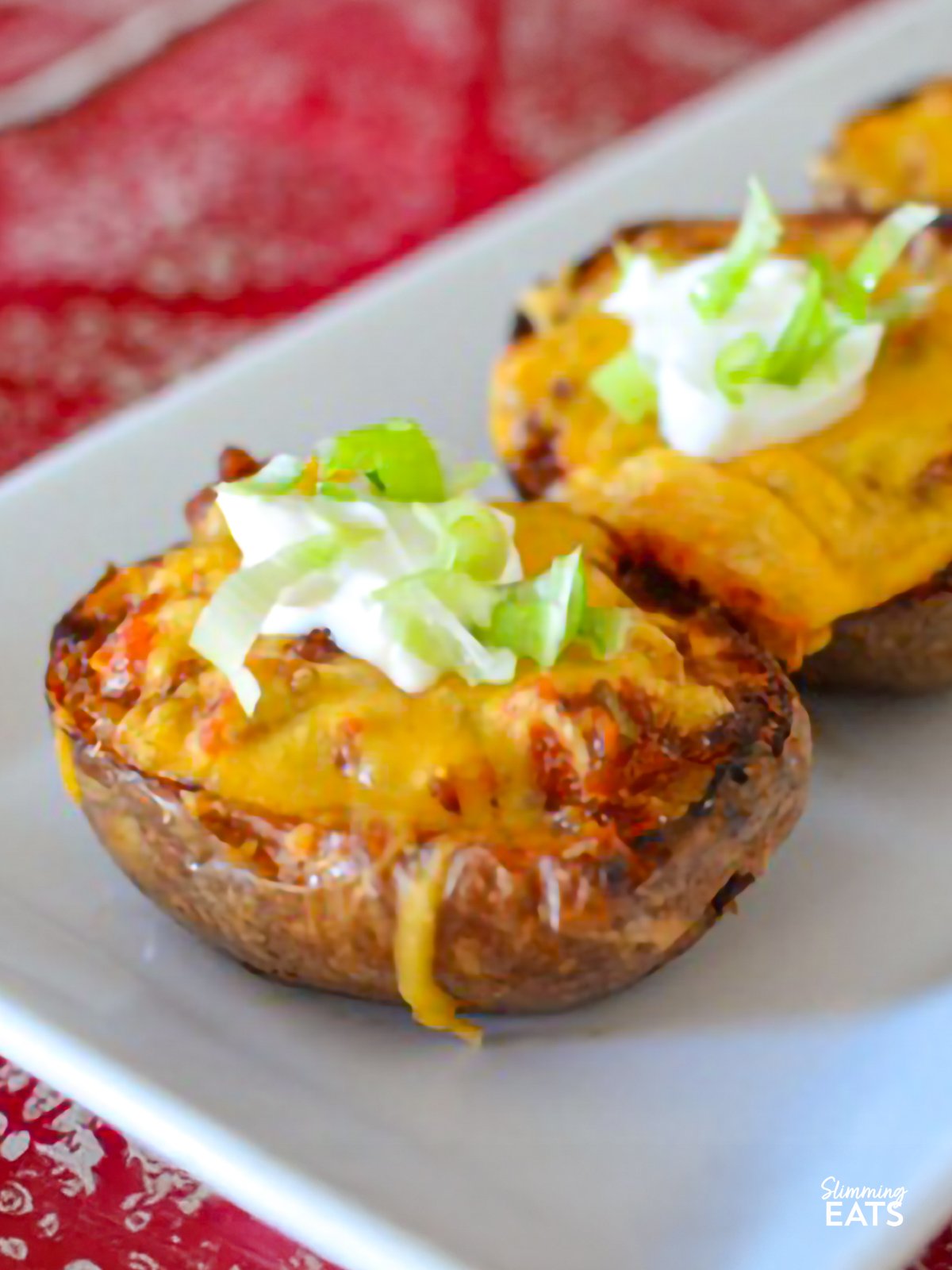 These Chilli Stuffed Potato Skins are a comforting and indulgent dish, with tender potato skins filled with flavour-packed chilli and topped with creamy soured cream. Perfect for a snack or a hearty meal, they’re sure to please everyone at the table. Chilli-Stuffed Potato Skins on a white rectangle plate place on a red patterned placemat