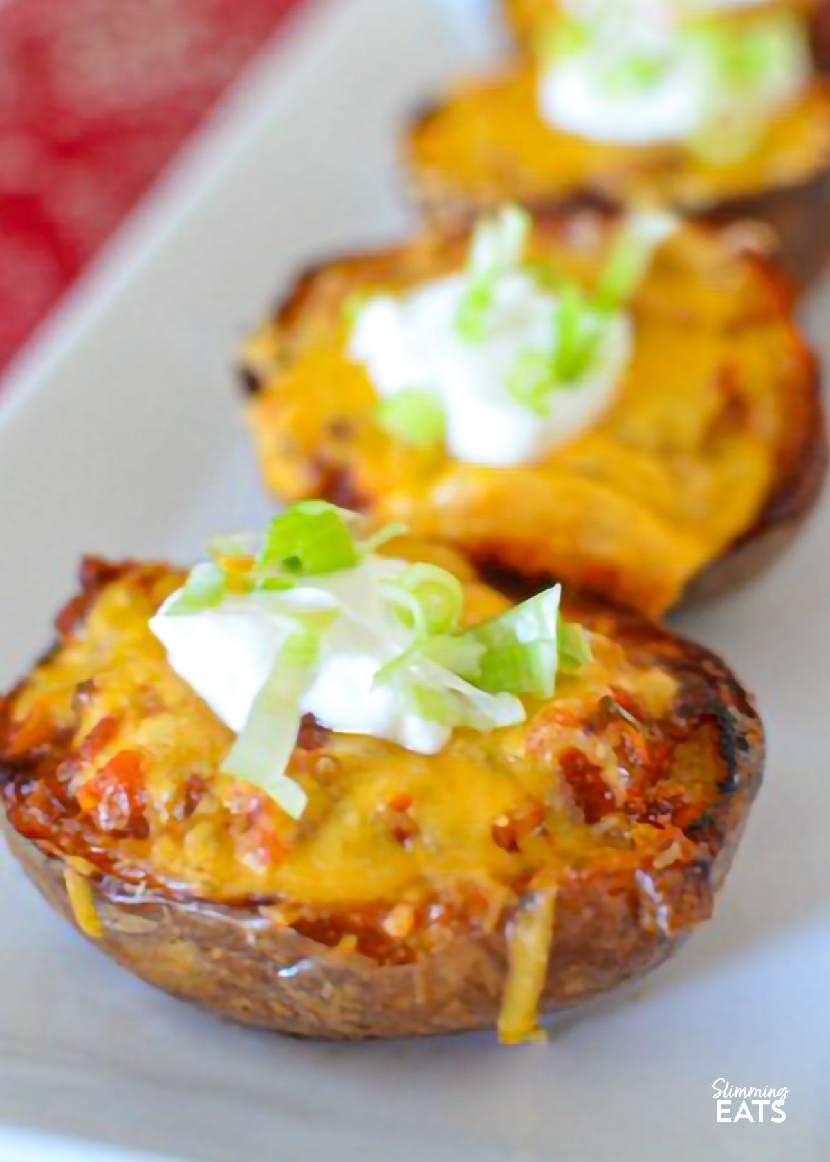 These Chilli Stuffed Potato Skins are a comforting and indulgent dish, with tender potato skins filled with flavour-packed chilli and topped with creamy soured cream. Perfect for a snack or a hearty meal, they’re sure to please everyone at the table. Chilli-Stuffed Potato Skins on a white rectangle plate place on a red patterned placemat