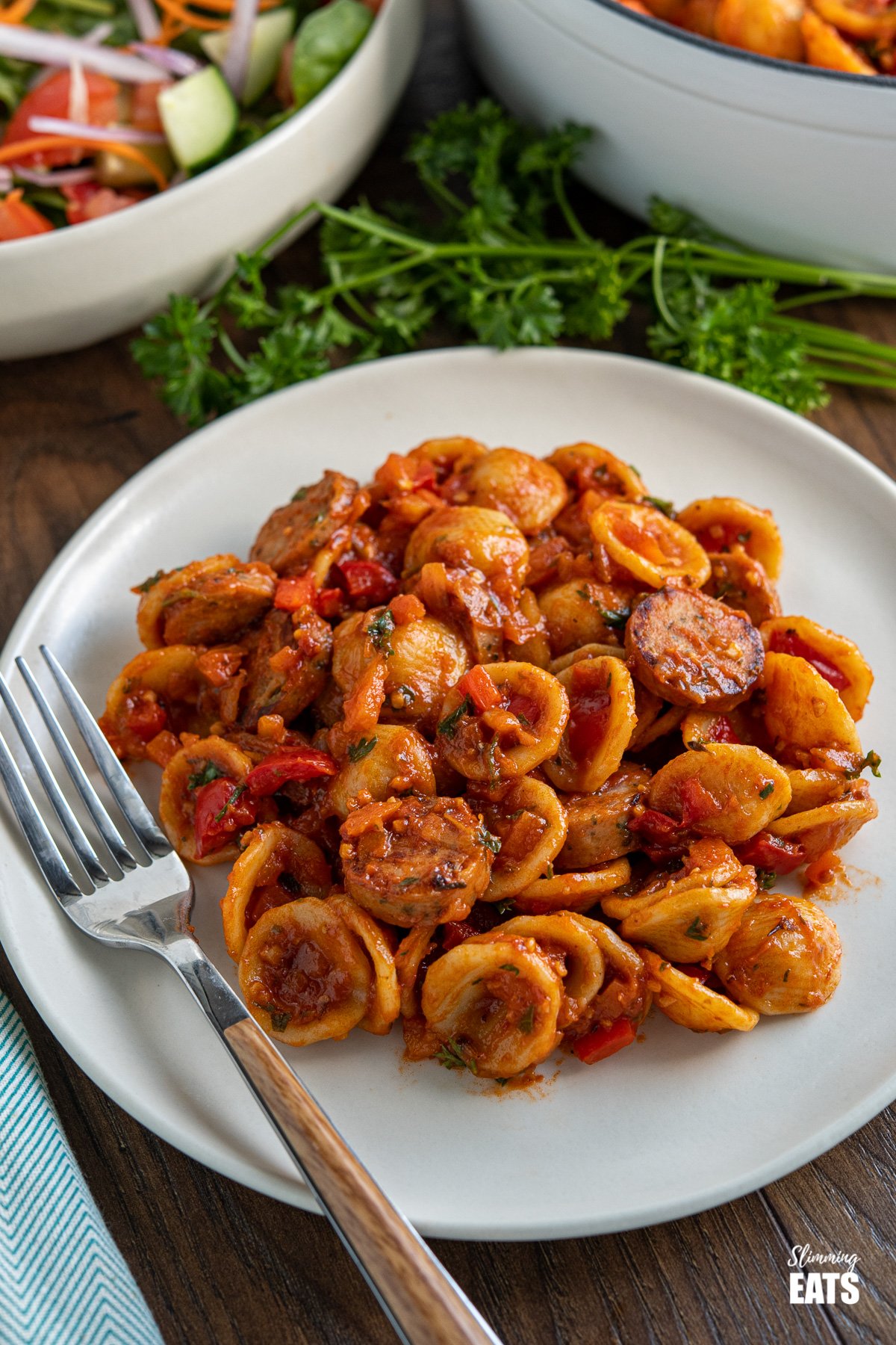 plate with smoked sausage orecchiette pasta and fork, salad in background