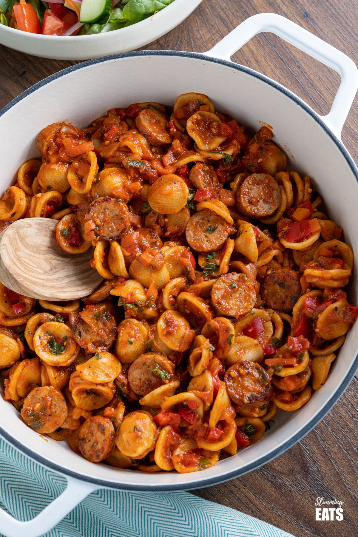 Orecchiette with Smoked Turkey Sausage - delicious bites of smoked sausage in rich tomato sauce with vegetables and orecchiette pasta. Slimming Eats and Weight Watchers friendly close up of Orecchiette with Smoked Turkey Sausage in a white cast iron skillet with olive wood spoon, salad in background