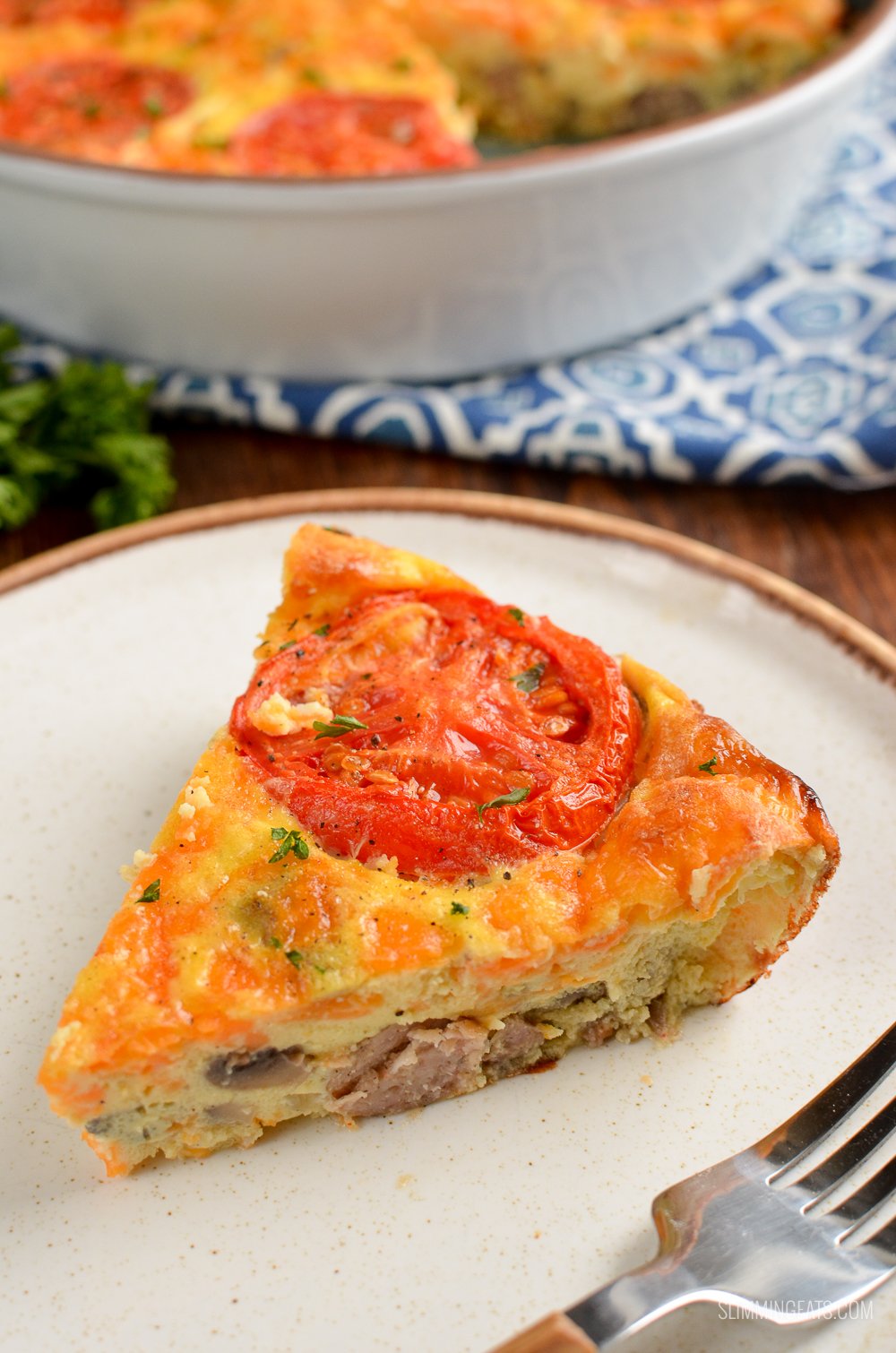 slice of breakfast quiche topped with tomato slice on a white plate