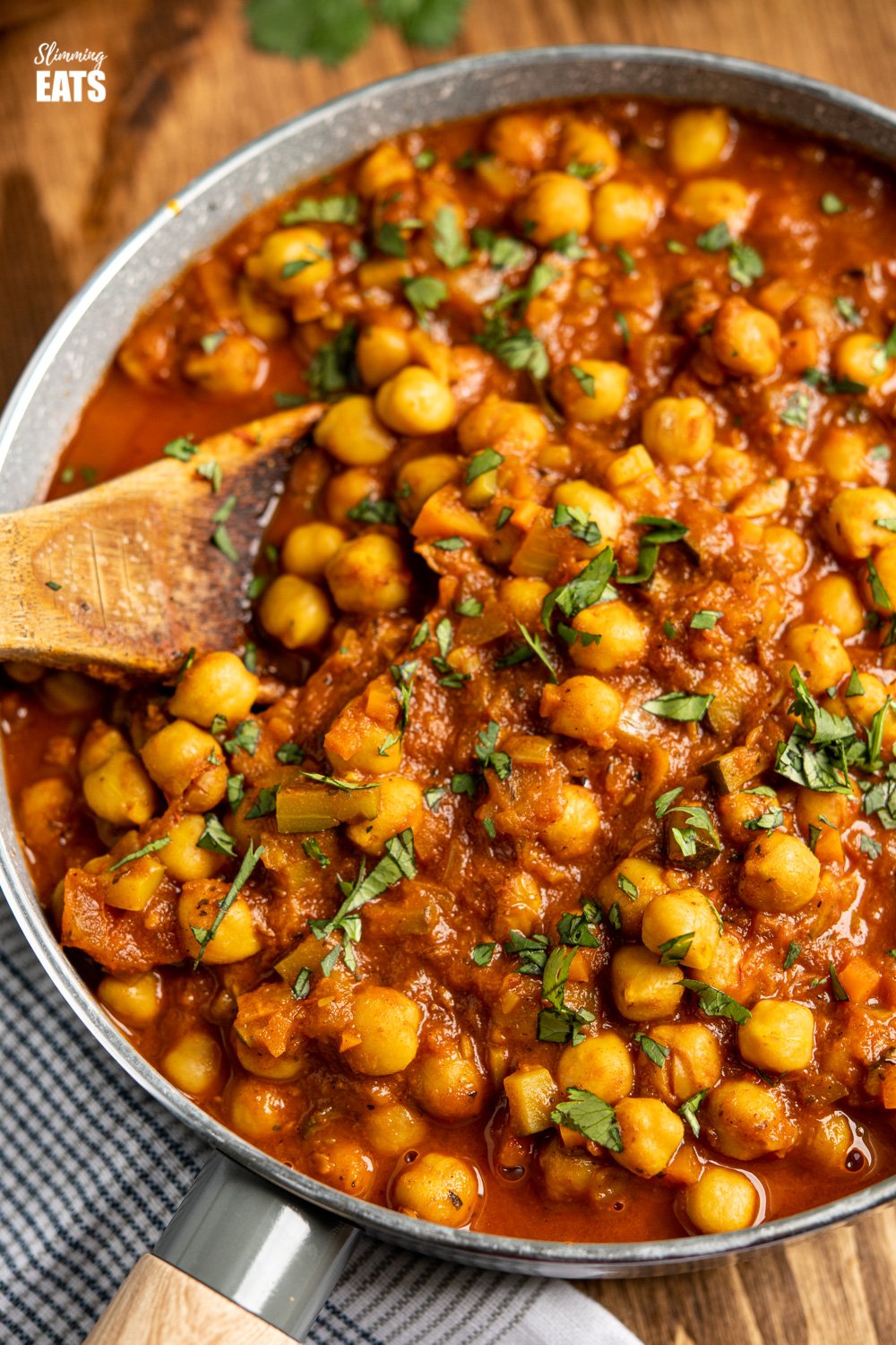 close up of Chana Masala in grey pan with wooden spoon of board 