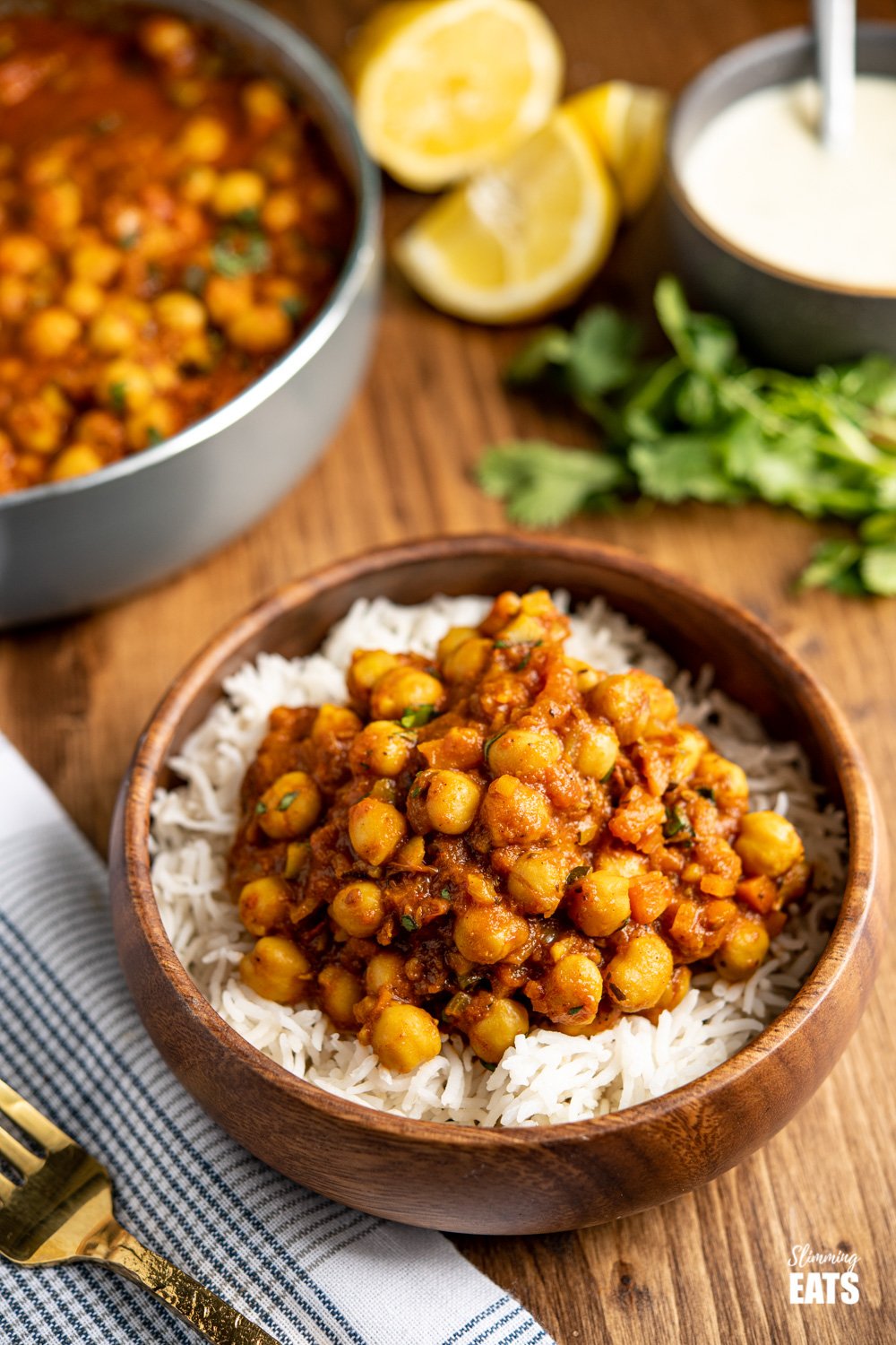 chana masala over white rice in a wooden bamboo bowl with gold fork to the left 