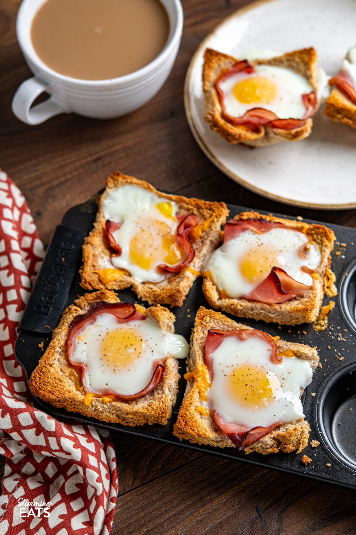 Egg, Ham and Cheese Toast Baskets in muffin tray with two toast cups on a plate with a cup of coffee