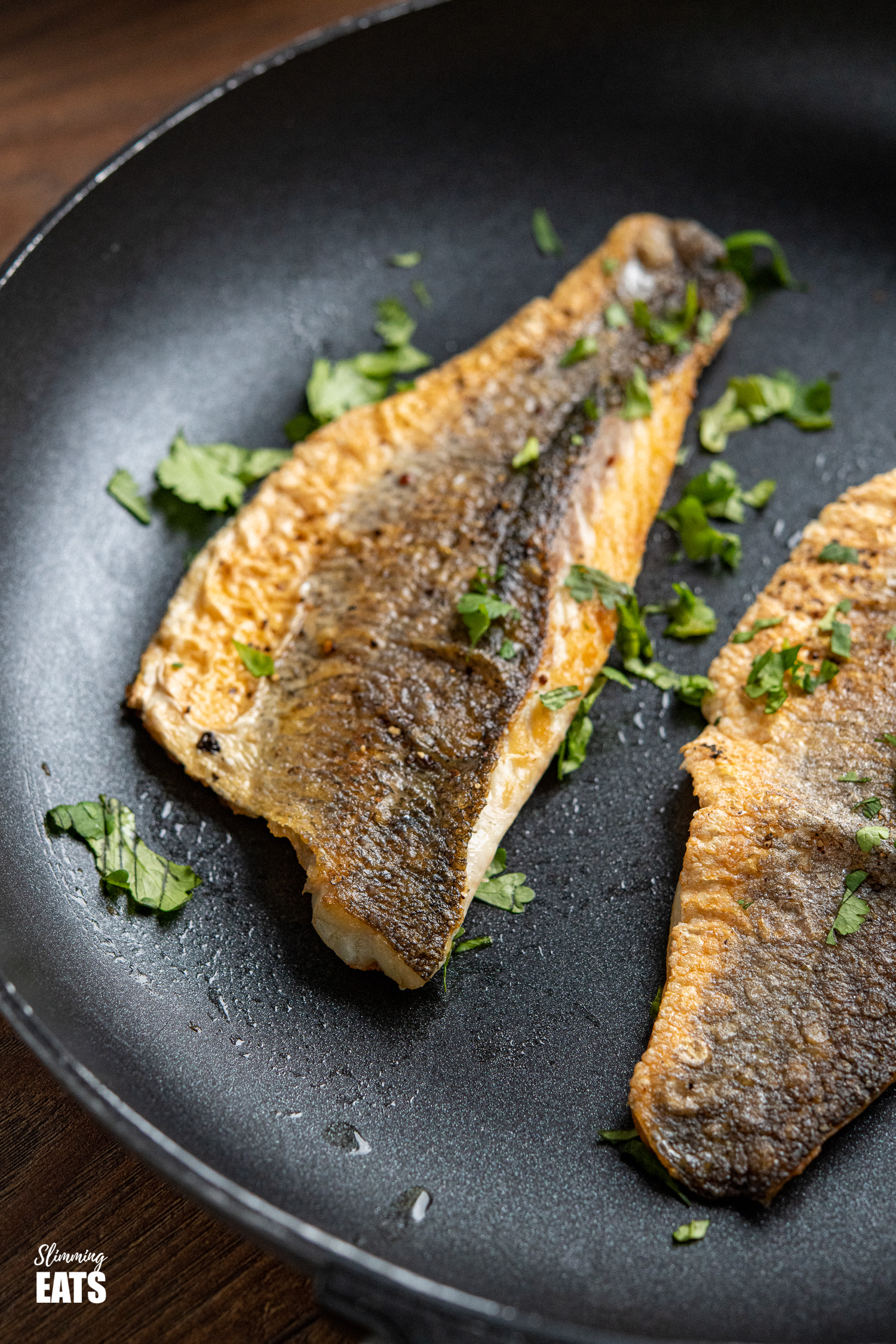 close up of Pan-fried Sea Bass fillets in frying pan with scattered chopped cilantro